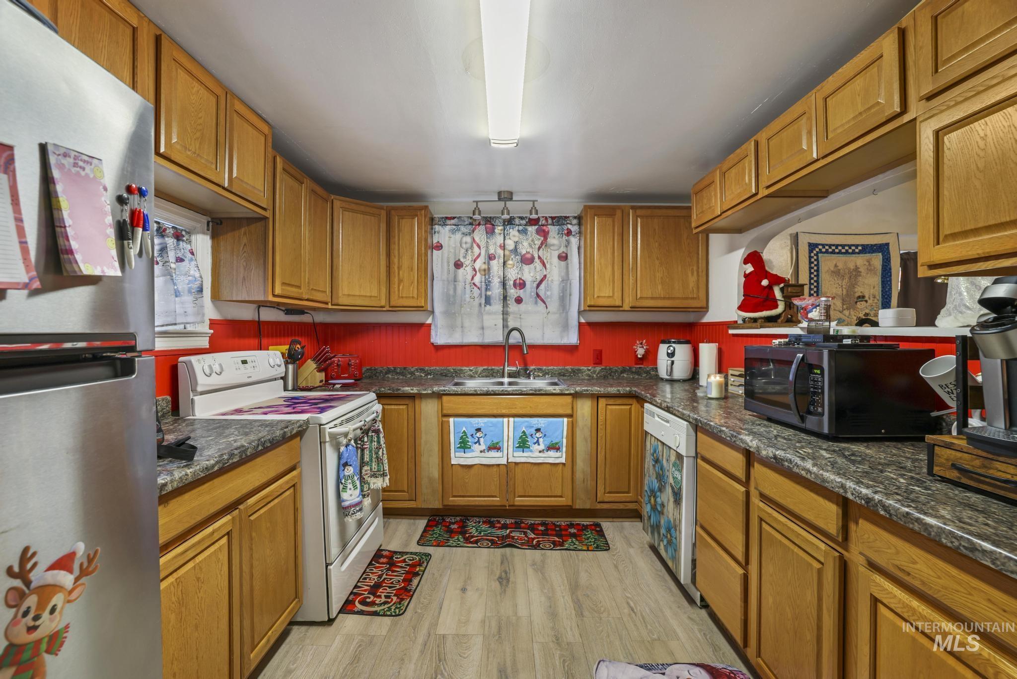 Kitchen with stainless steel appliances, brown cabinets, light wood-type flooring, and dark stone countertops