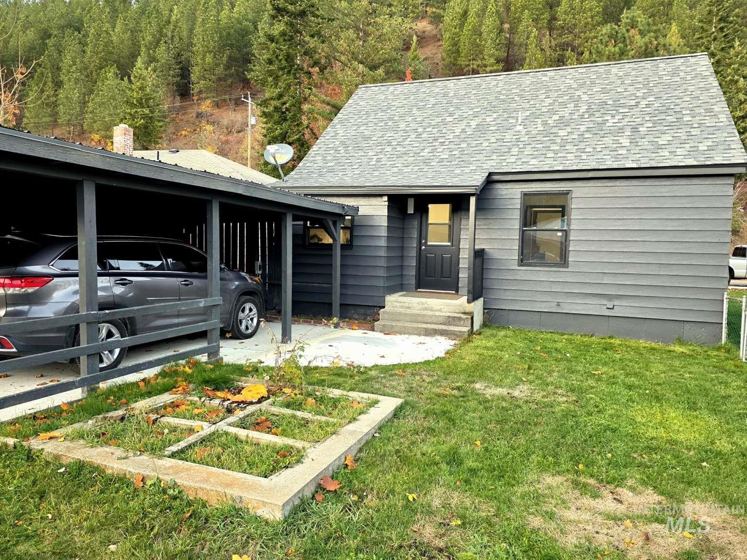 View of front of house with a front yard, a garden, a shingled roof, and a wooded view
