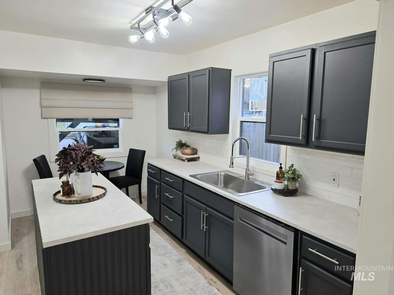 Kitchen featuring light countertops, stainless steel dishwasher, tasteful backsplash, a kitchen island, and light wood-type flooring
