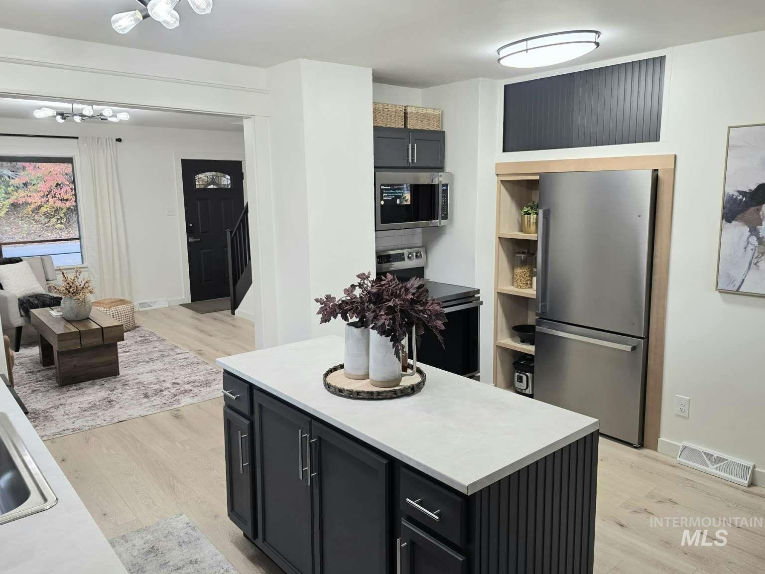 Kitchen featuring dark cabinetry, stainless steel appliances, light wood-style floors, light countertops, and a center island