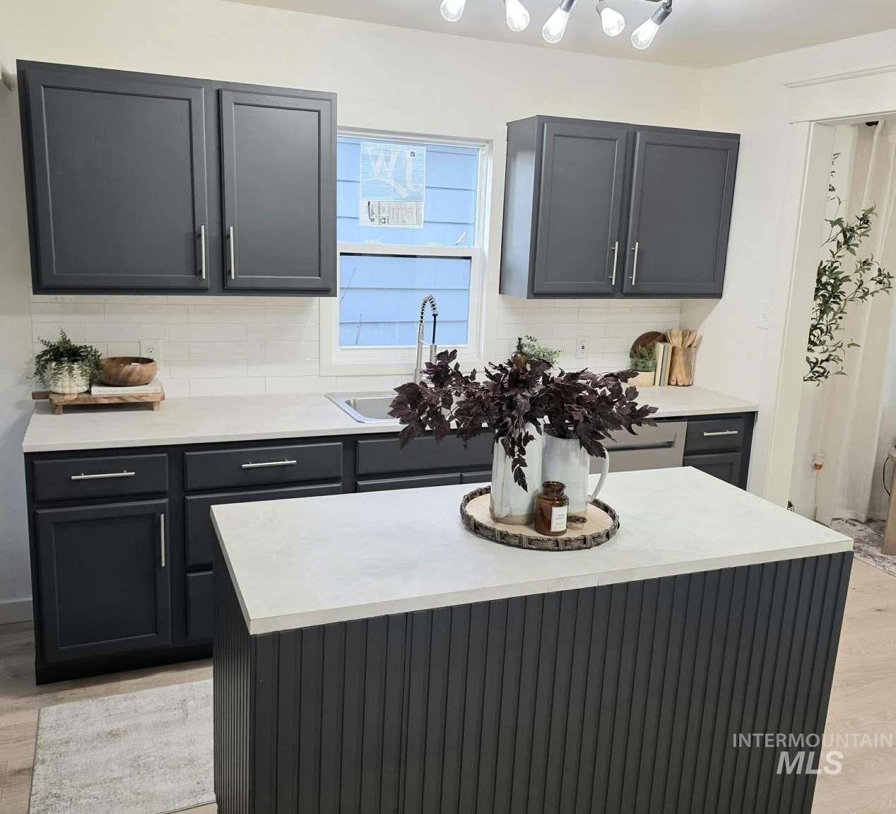 Kitchen featuring light wood finished floors, decorative backsplash, light countertops, and a kitchen island