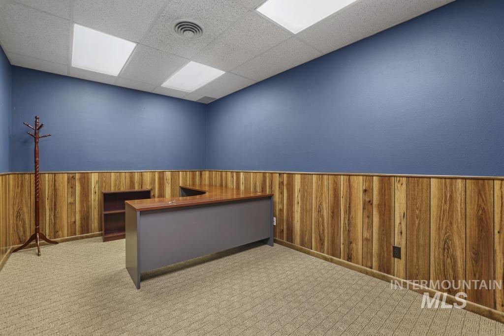 Unfurnished office featuring wooden walls, wainscoting, light colored carpet, and a drop ceiling