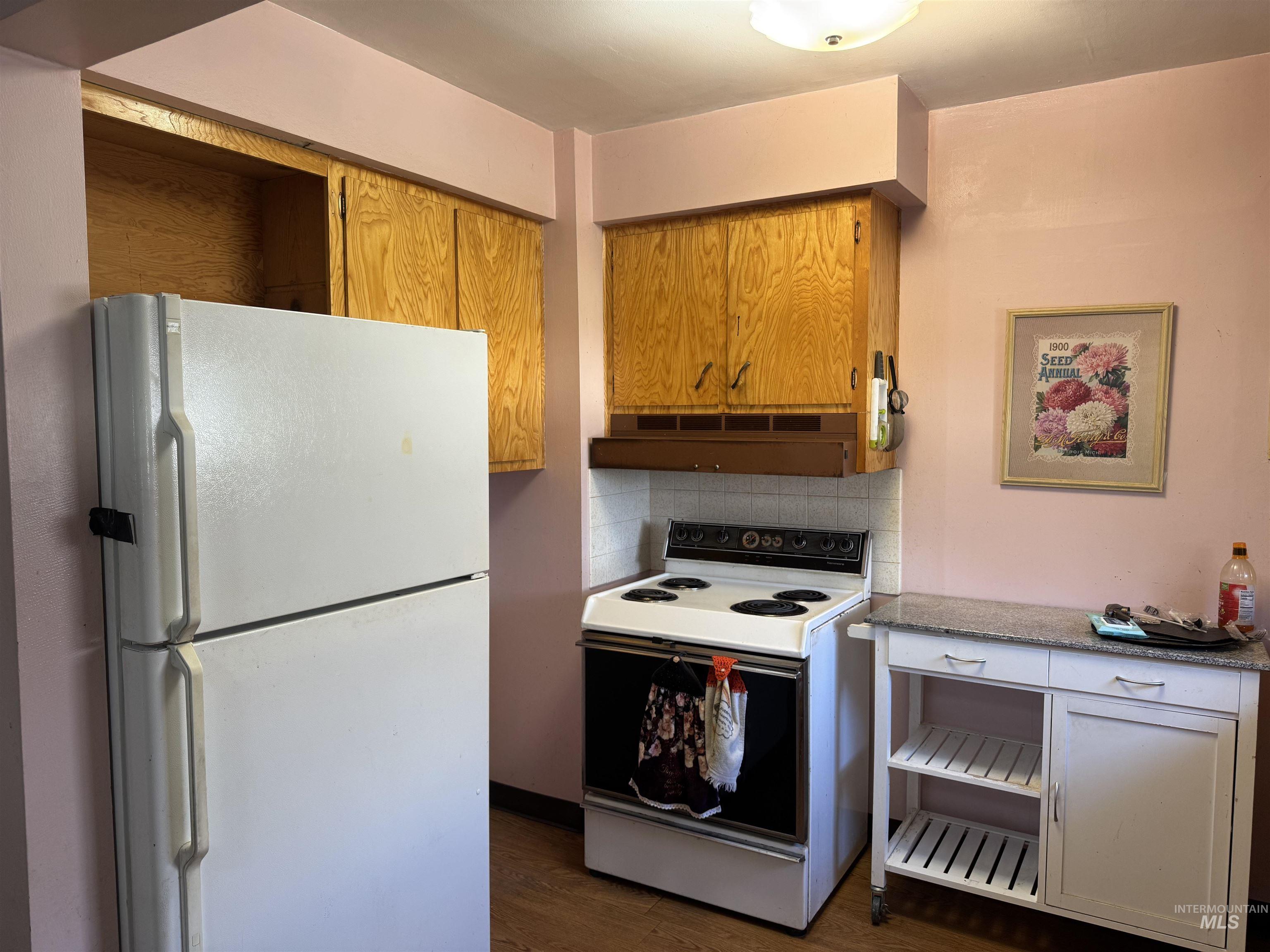 Kitchen featuring white appliances, tasteful backsplash, dark wood-style floors, extractor fan, and brown cabinetry