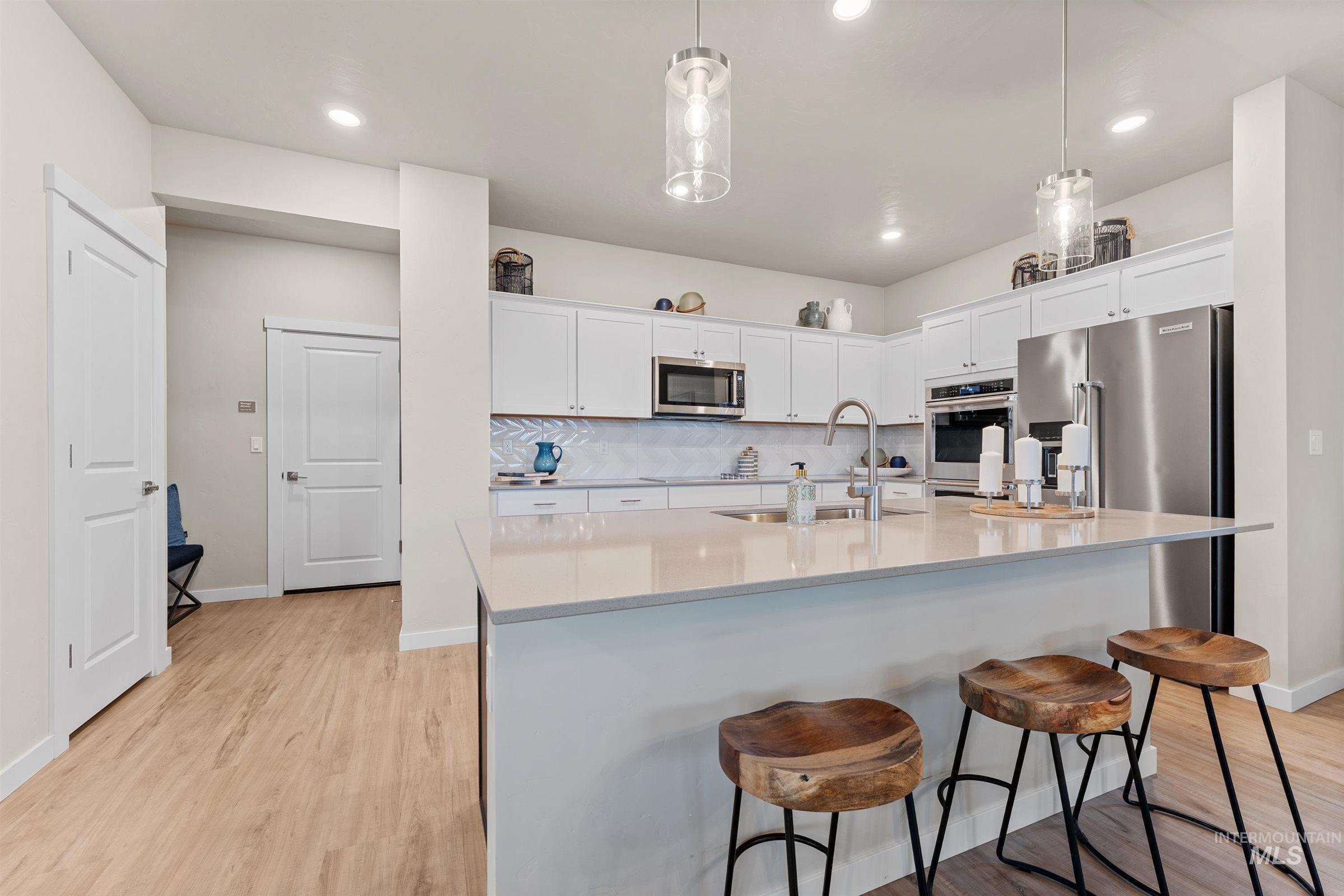 Kitchen with decorative backsplash, light wood-type flooring, white cabinets, pendant lighting, and a breakfast bar