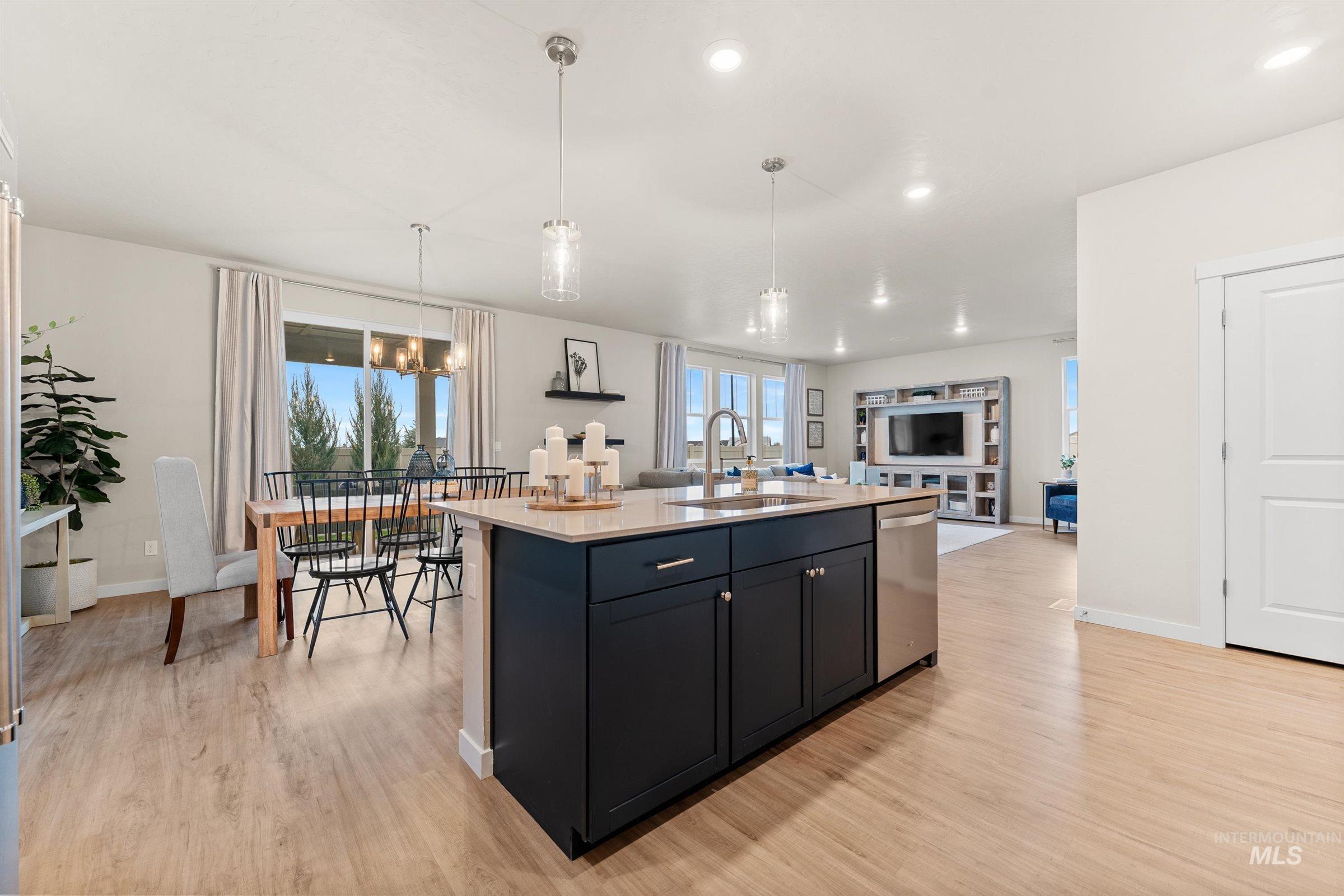 Kitchen featuring decorative light fixtures, a center island with sink, light wood-style floors, dark cabinets, and open floor plan