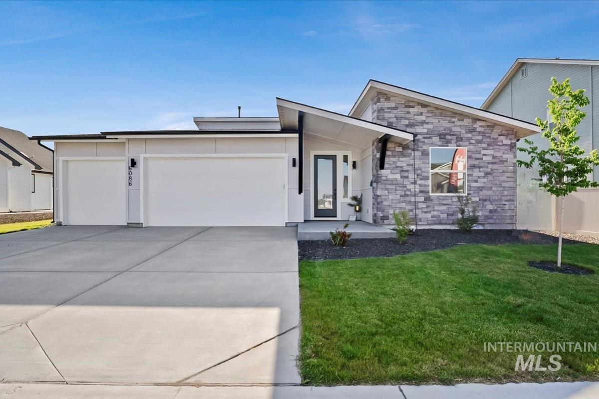 View of front facade with a front yard, stone siding, an attached garage, and driveway