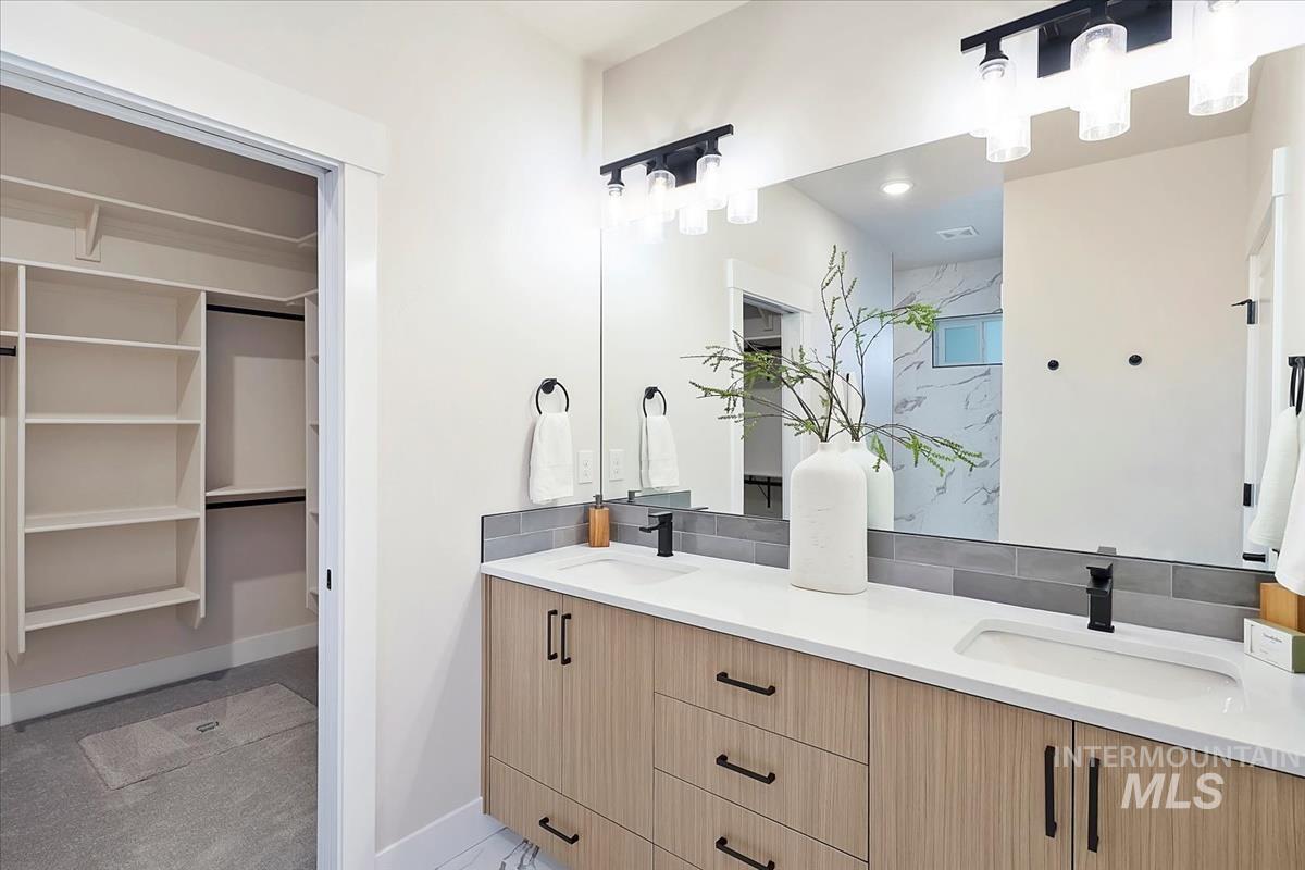 Full bathroom featuring double vanity, tasteful backsplash, recessed lighting, a spacious closet, and a marble finish shower