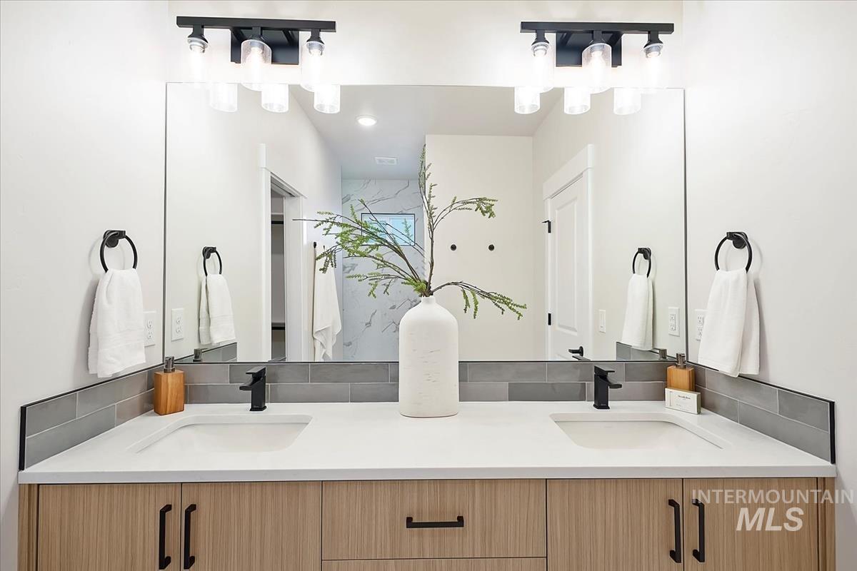 Bathroom with double vanity, a chandelier, and tasteful backsplash