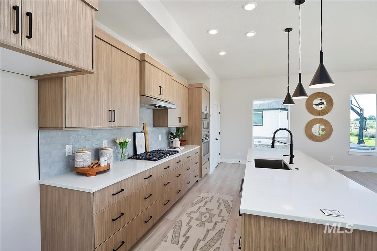 Kitchen with light brown cabinetry, plenty of natural light, light wood-style floors, tasteful backsplash, and recessed lighting