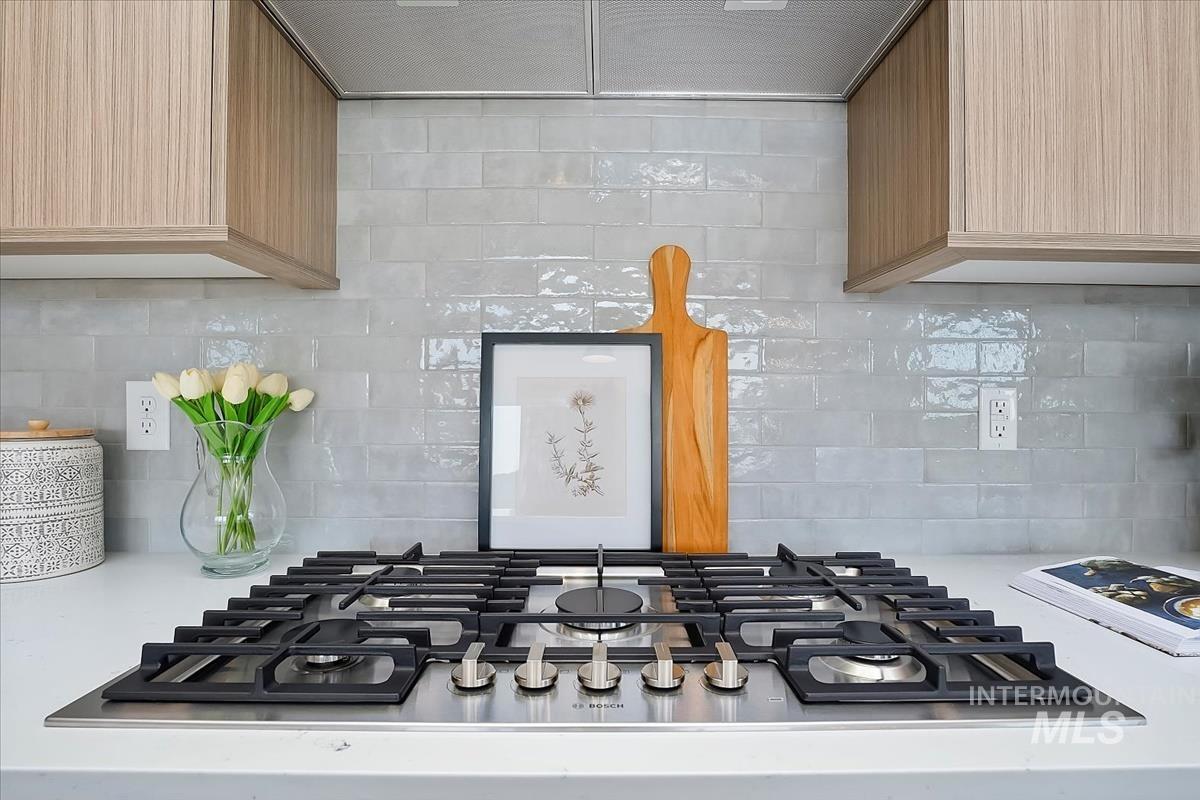 Kitchen view of backsplash, ventilation hood, stainless steel gas stovetop, and light stone counters