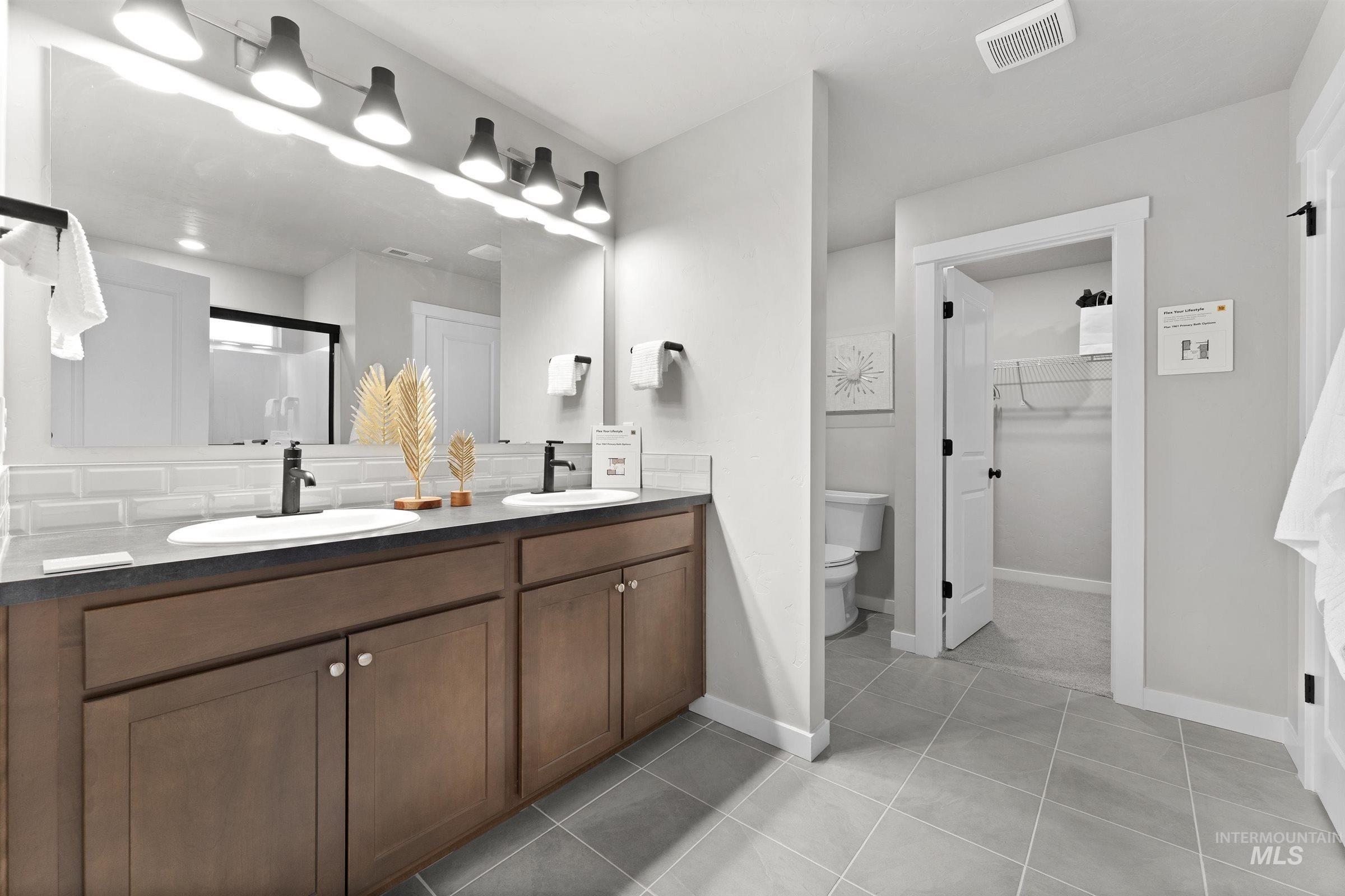 Full bathroom featuring a shower stall, double vanity, light tile patterned floors, a walk in closet, and decorative backsplash