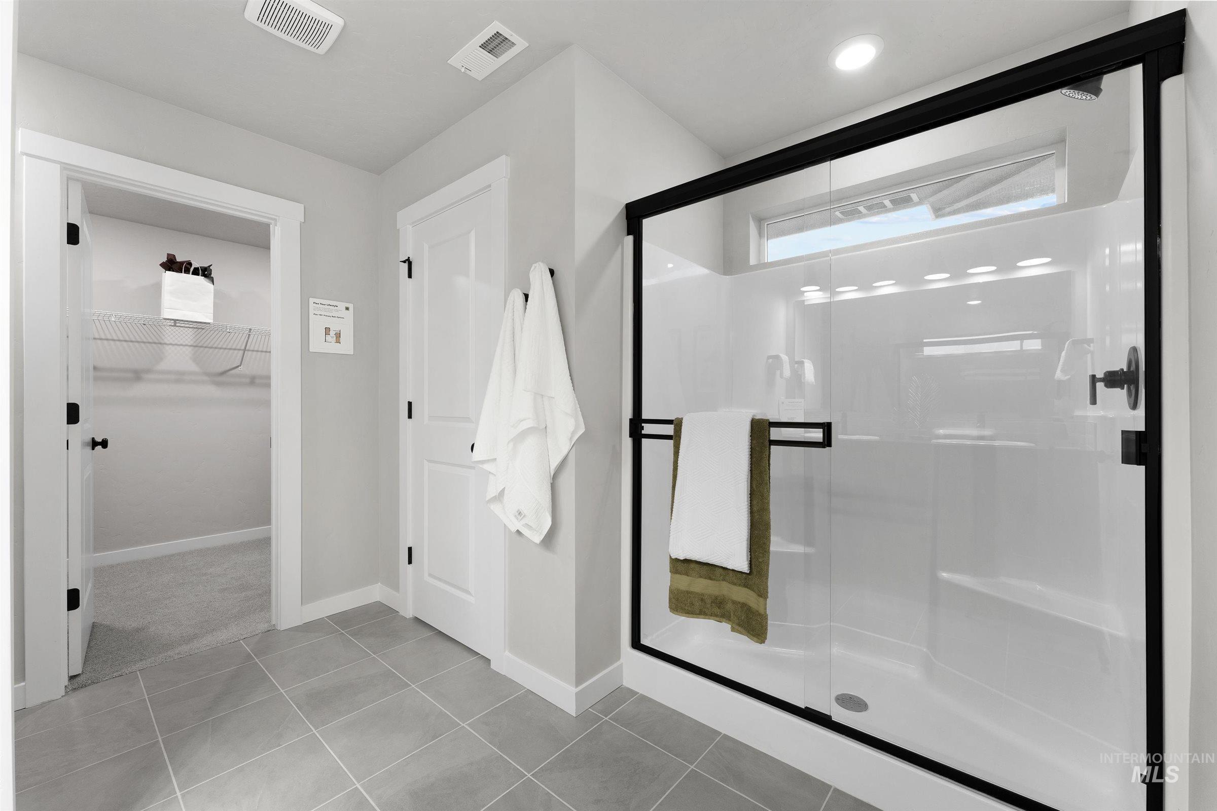 Bathroom with a spacious closet, a stall shower, and light tile patterned floors