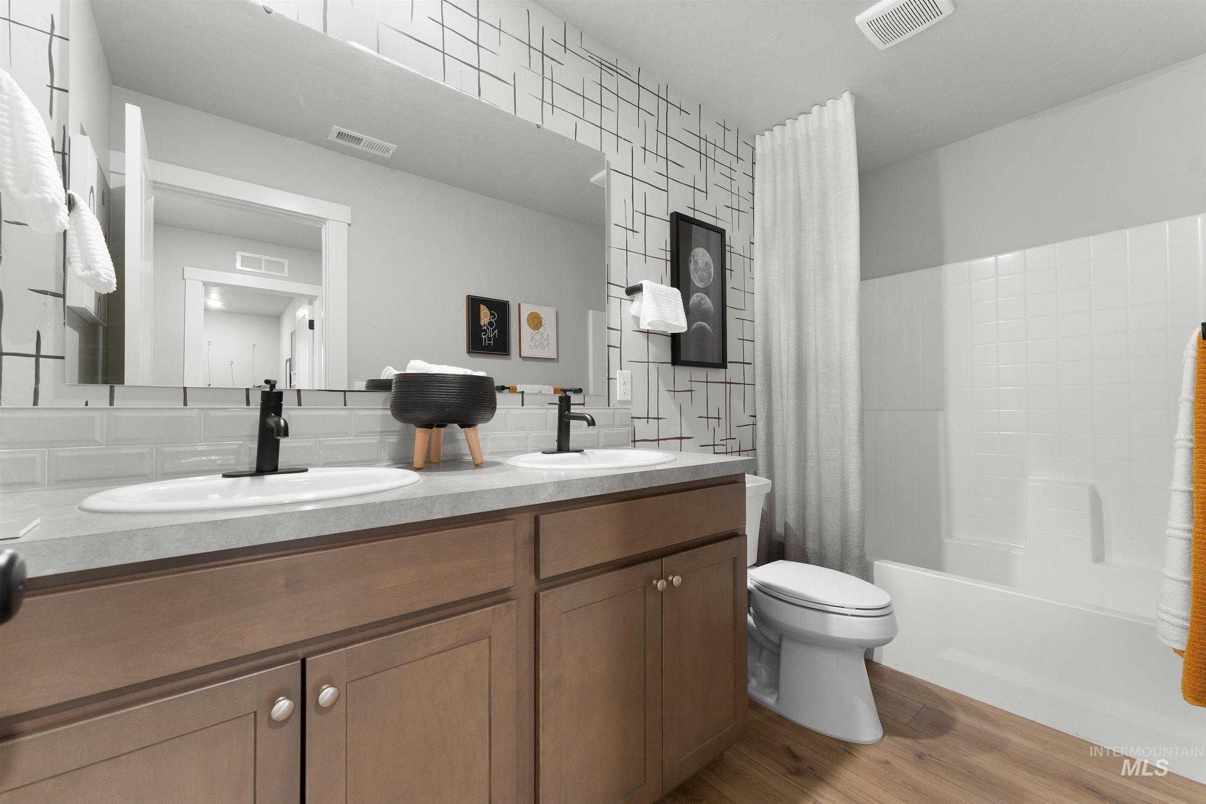 Bathroom with light wood-type flooring, double vanity, and shower / bath combination with curtain