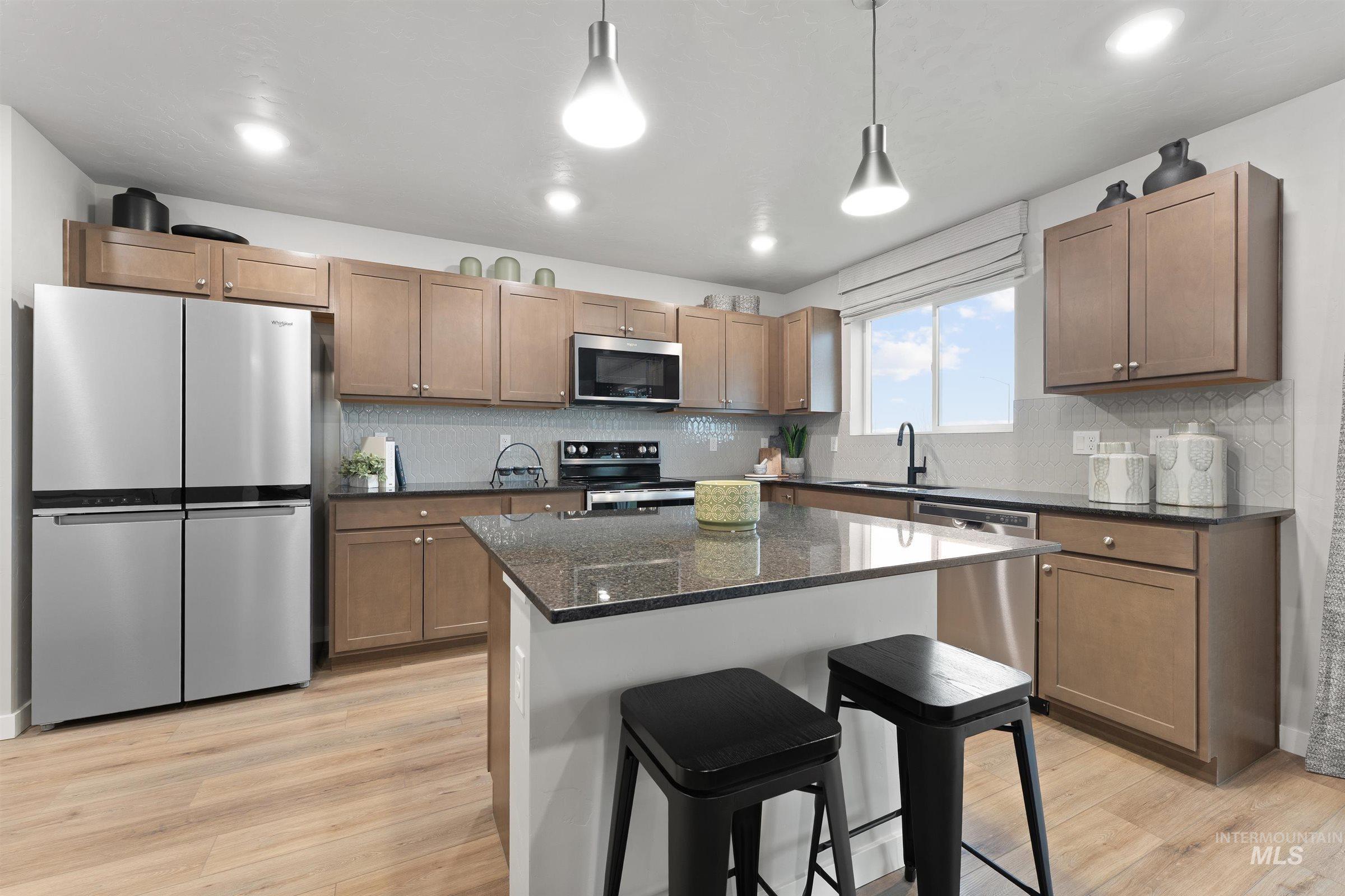 Kitchen featuring a kitchen breakfast bar, appliances with stainless steel finishes, decorative backsplash, hanging light fixtures, and light wood-style floors