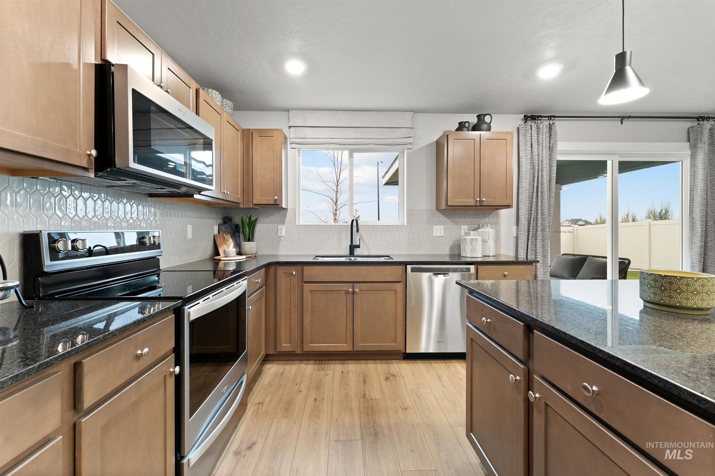 Kitchen featuring stainless steel appliances, dark stone counters, backsplash, and light wood-type flooring