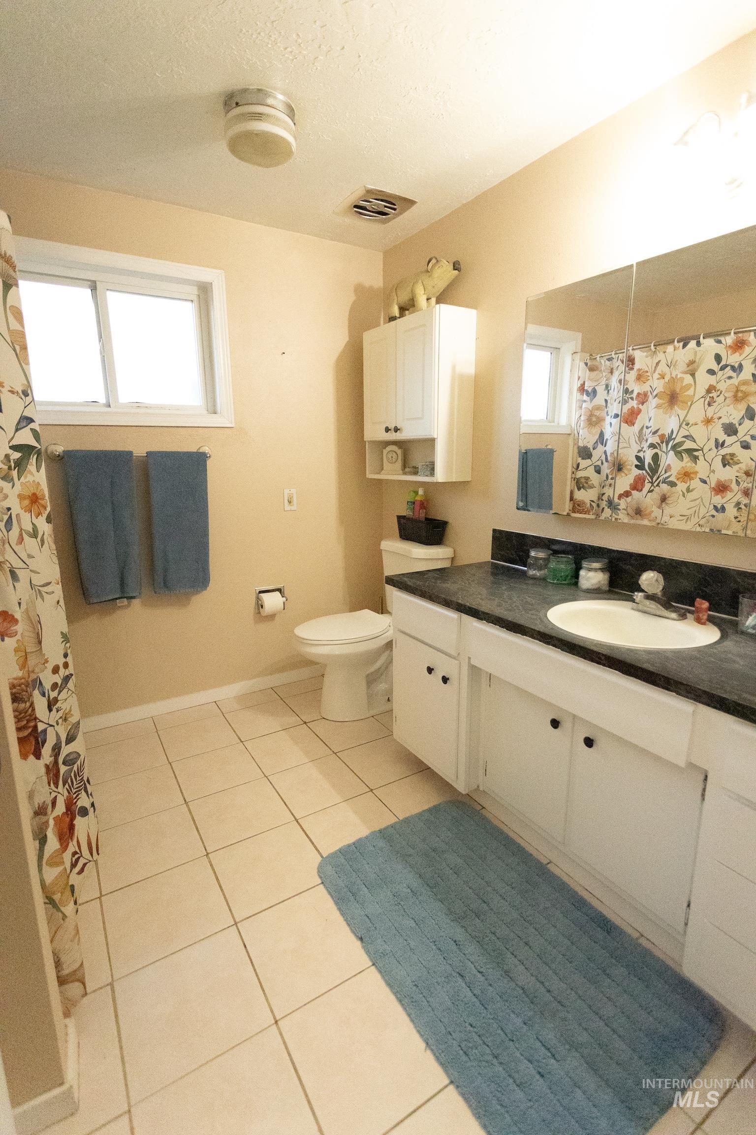 Bathroom featuring a shower with shower curtain, light tile patterned floors, vanity, and a textured ceiling