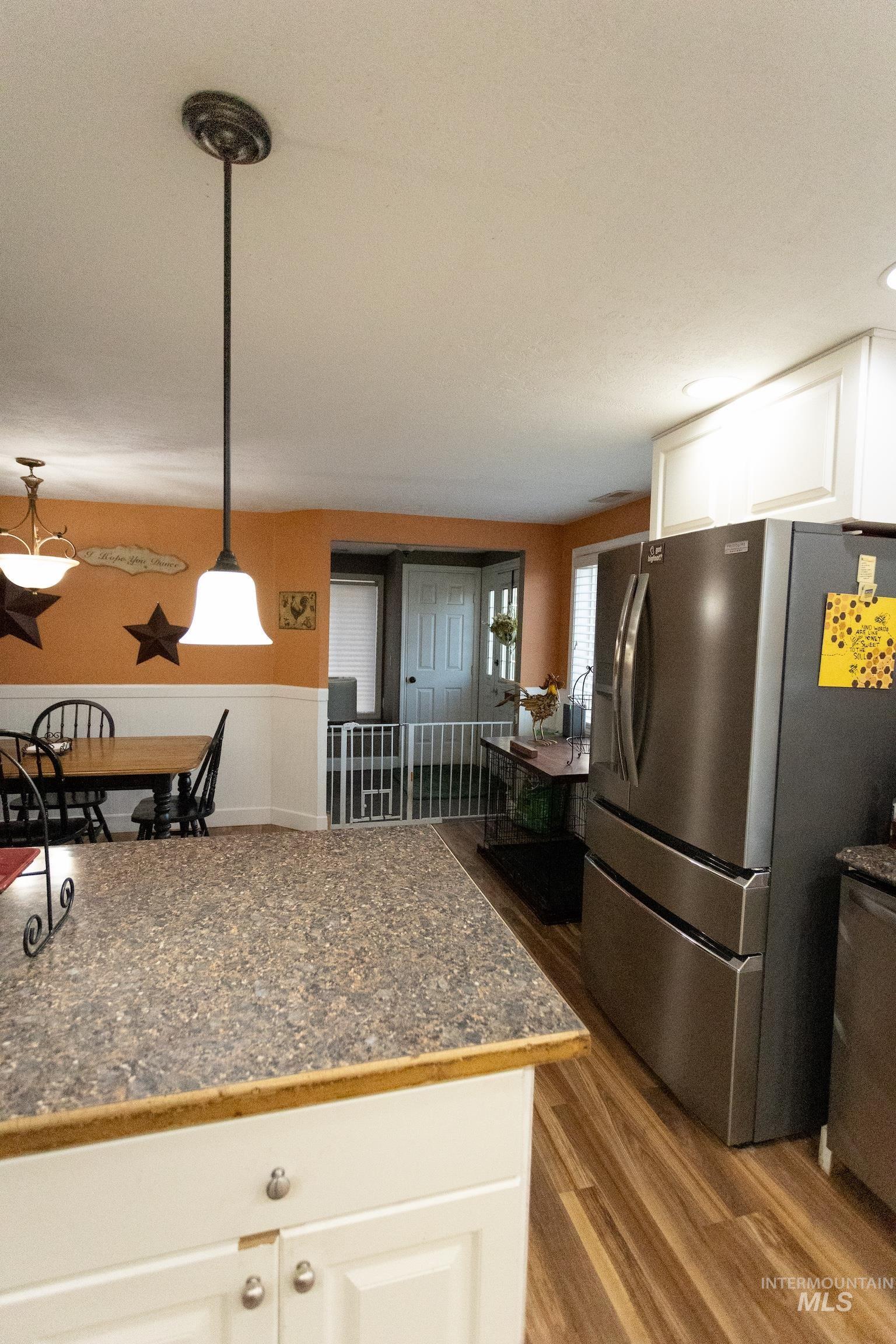 Kitchen with white cabinets, stainless steel fridge with ice dispenser, dark countertops, dark wood-style floors, and pendant lighting