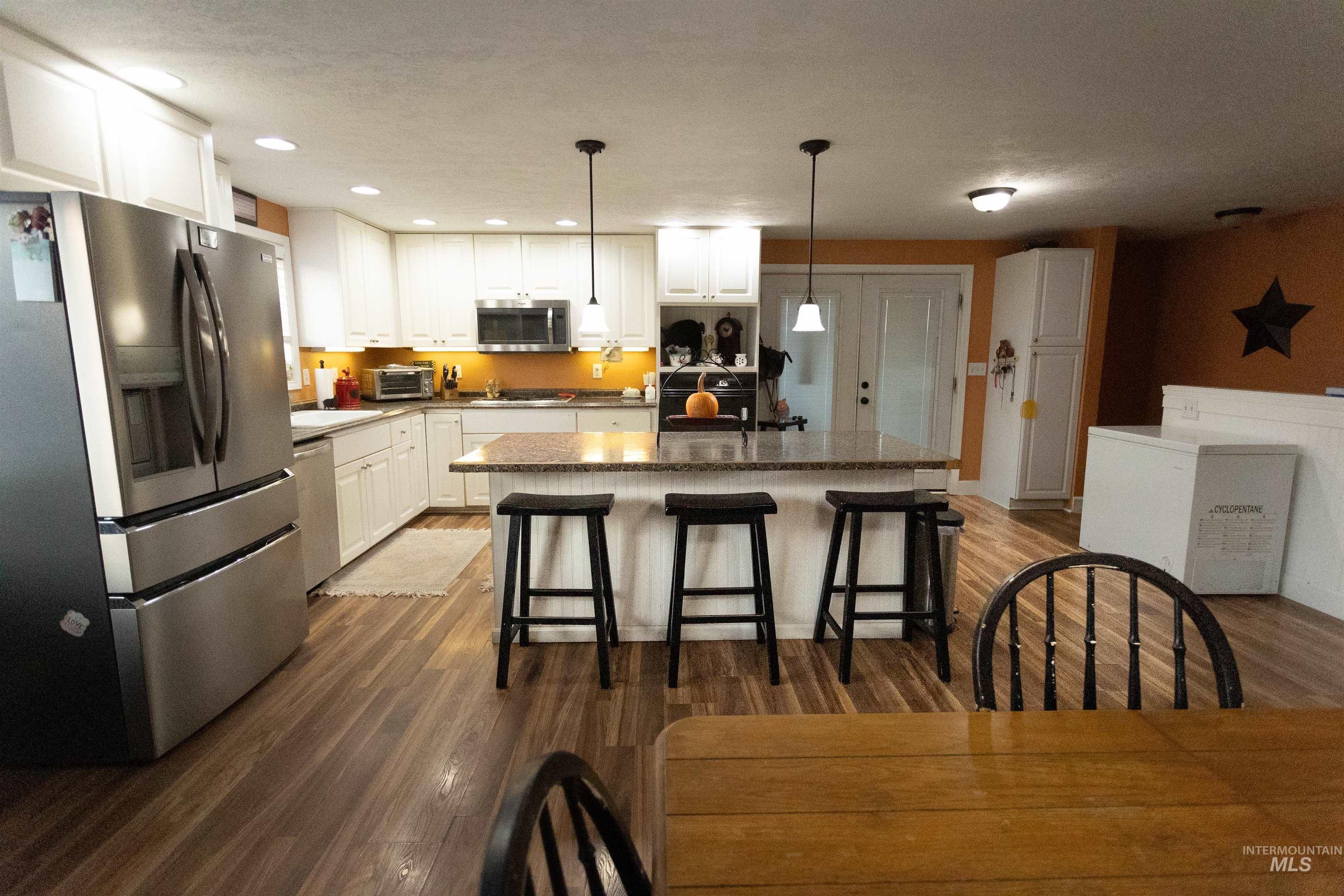 Kitchen with appliances with stainless steel finishes, dark wood finished floors, a center island with sink, white cabinets, and recessed lighting