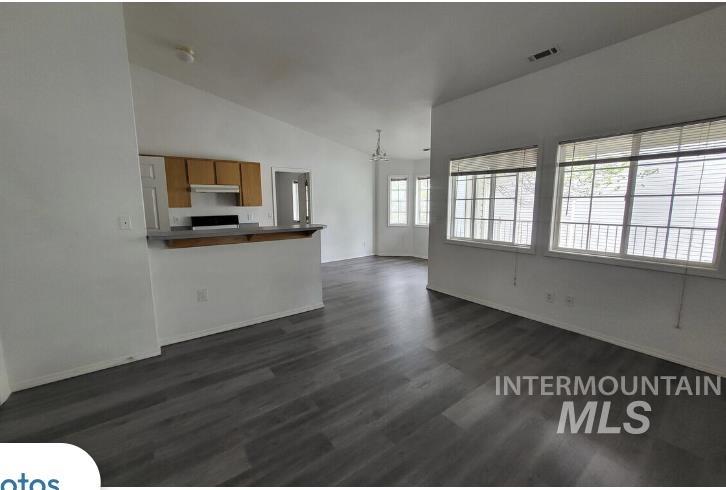 Unfurnished living room with vaulted ceiling, dark wood-style flooring, and a chandelier