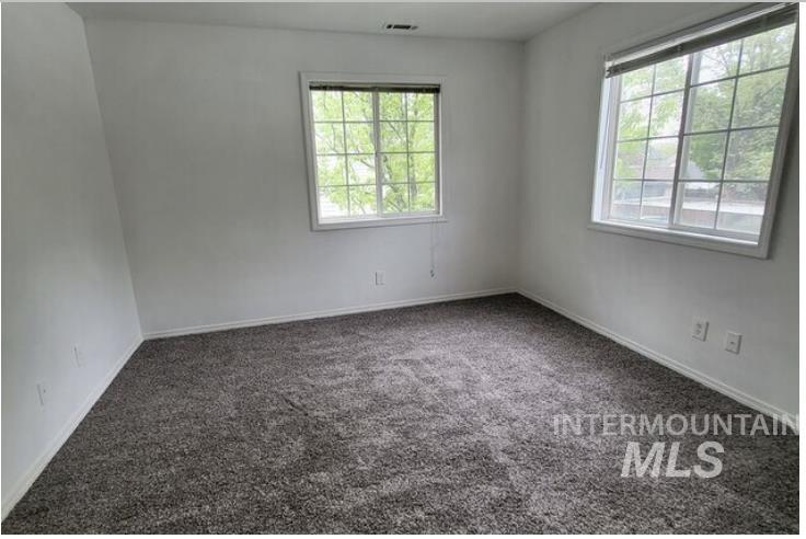 Spare room featuring dark colored carpet and plenty of natural light