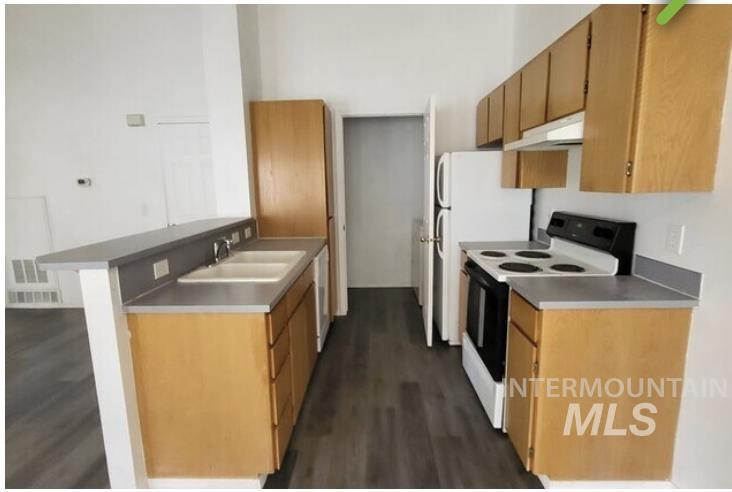 Kitchen featuring electric range, a peninsula, dark wood-style flooring, under cabinet range hood, and brown cabinetry