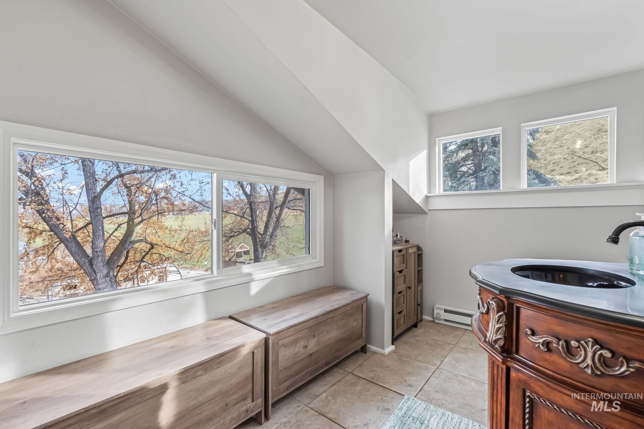 Interior space featuring light tile patterned flooring, a baseboard heating unit, and vaulted ceiling