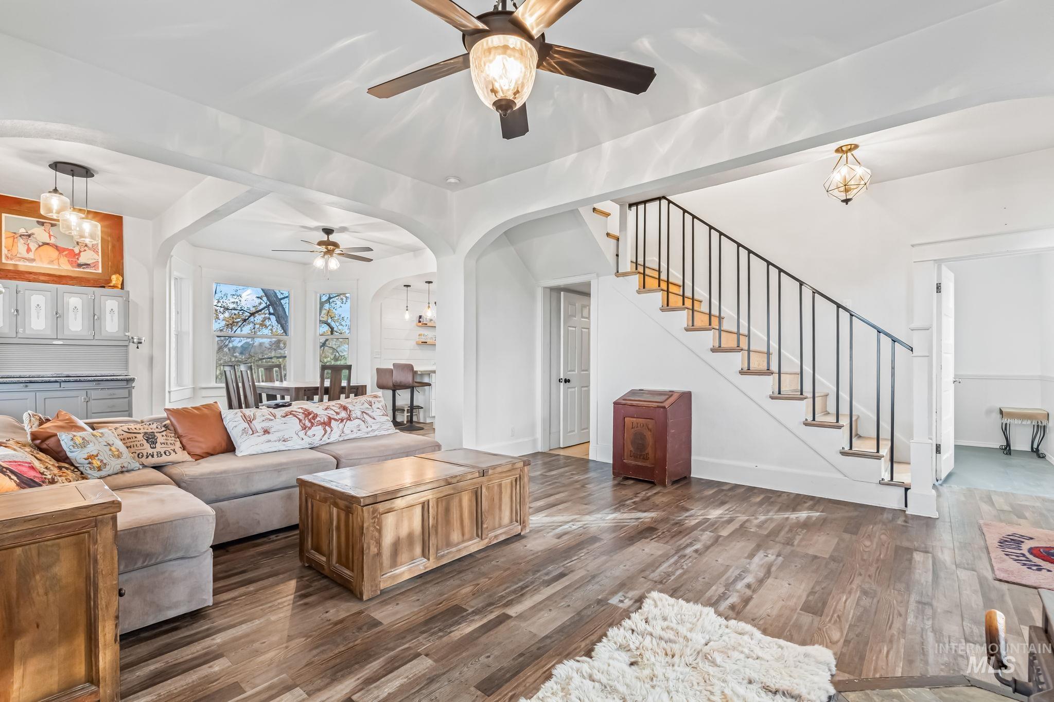 Living area featuring a chandelier, dark wood finished floors, arched walkways, ceiling fan, and stairs