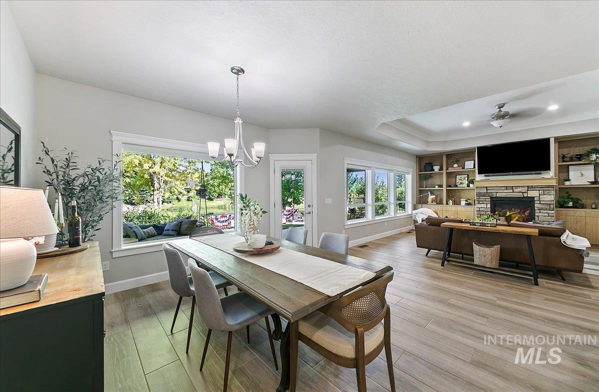 Dining room featuring light wood finished floors, a fireplace, a tray ceiling, built in shelves, and recessed lighting