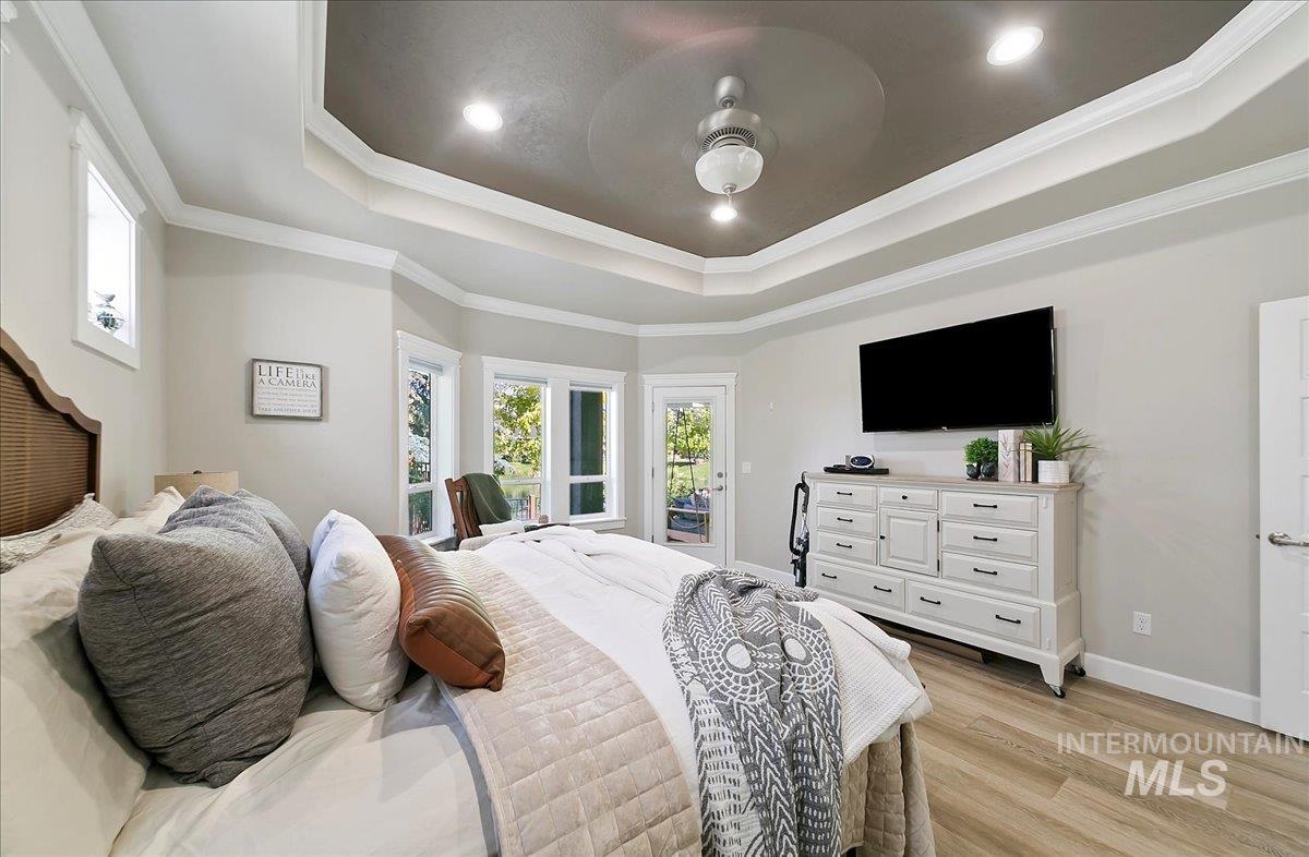 Bedroom with light wood-style floors, ornamental molding, recessed lighting, access to exterior, and a tray ceiling