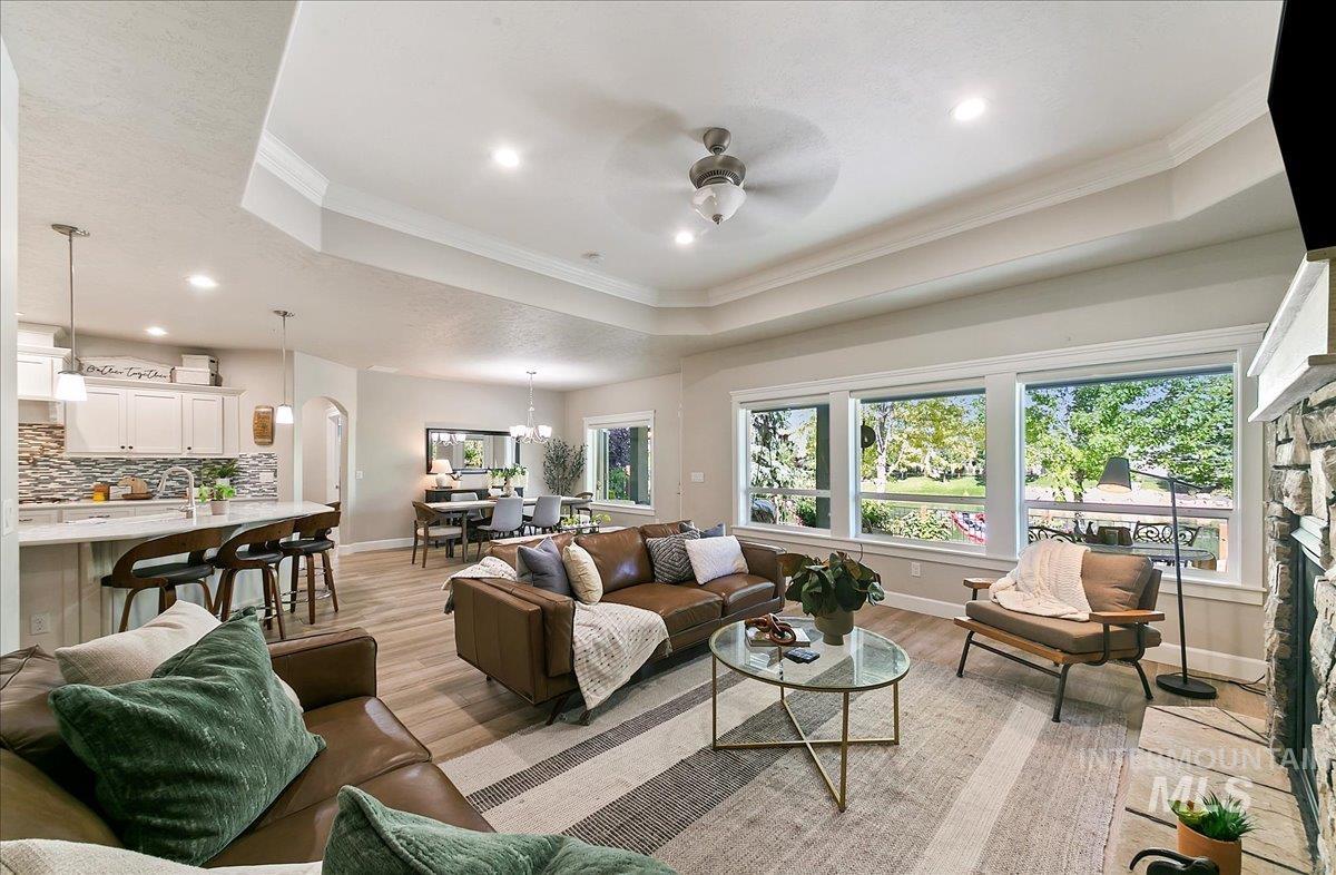 Living room with ceiling fan, crown molding, recessed lighting, light wood-type flooring, and a stone fireplace