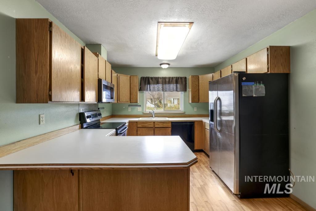 Kitchen featuring stainless steel appliances, a peninsula, light countertops, a textured ceiling, and light wood finished floors
