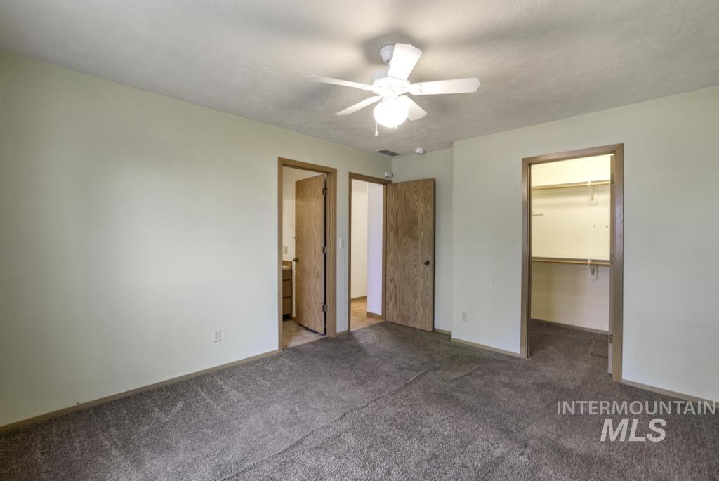 Unfurnished bedroom featuring a spacious closet, carpet floors, ceiling fan, and ensuite bathroom
