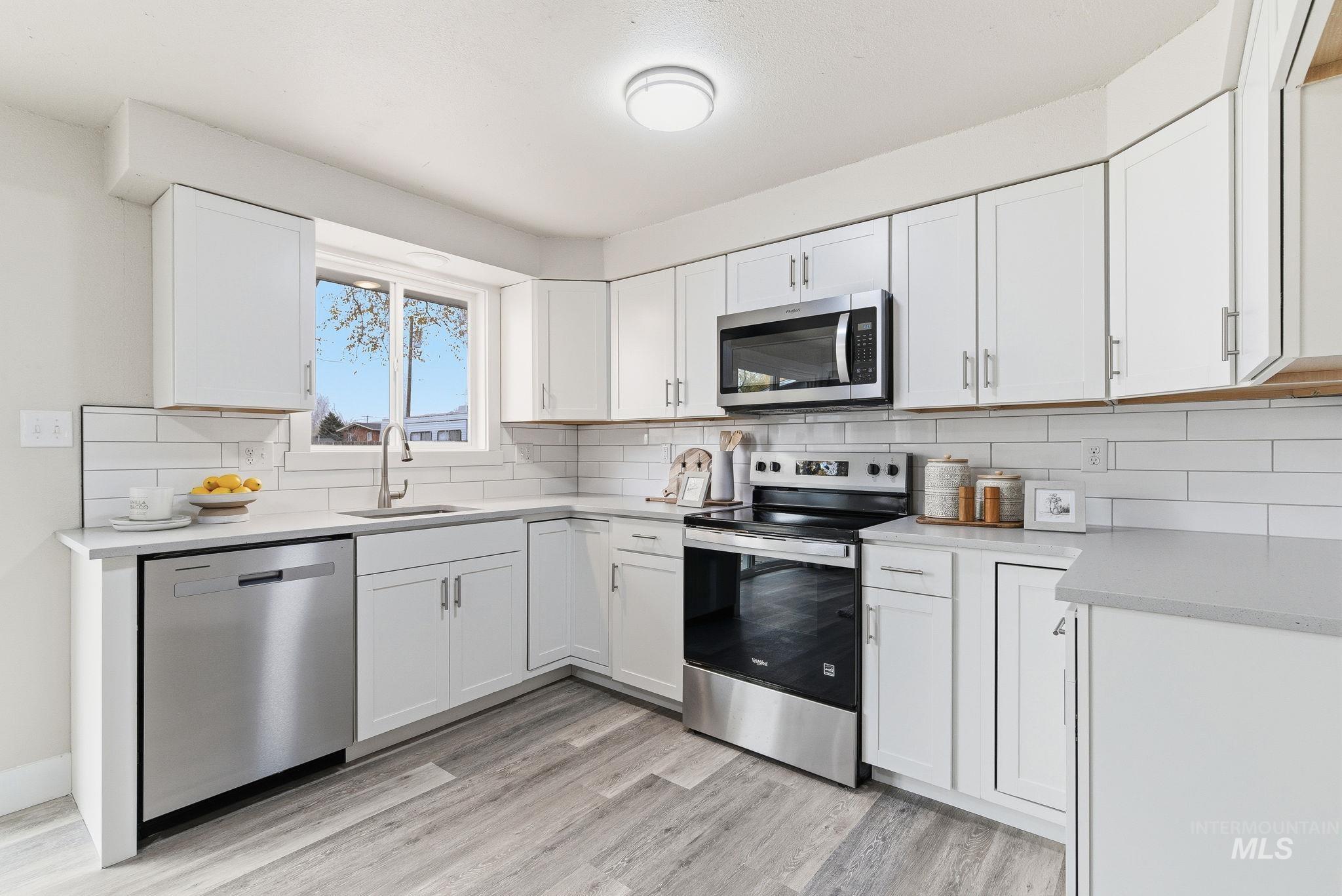 Kitchen with appliances with stainless steel finishes, white cabinets, decorative backsplash, and light wood-style floors