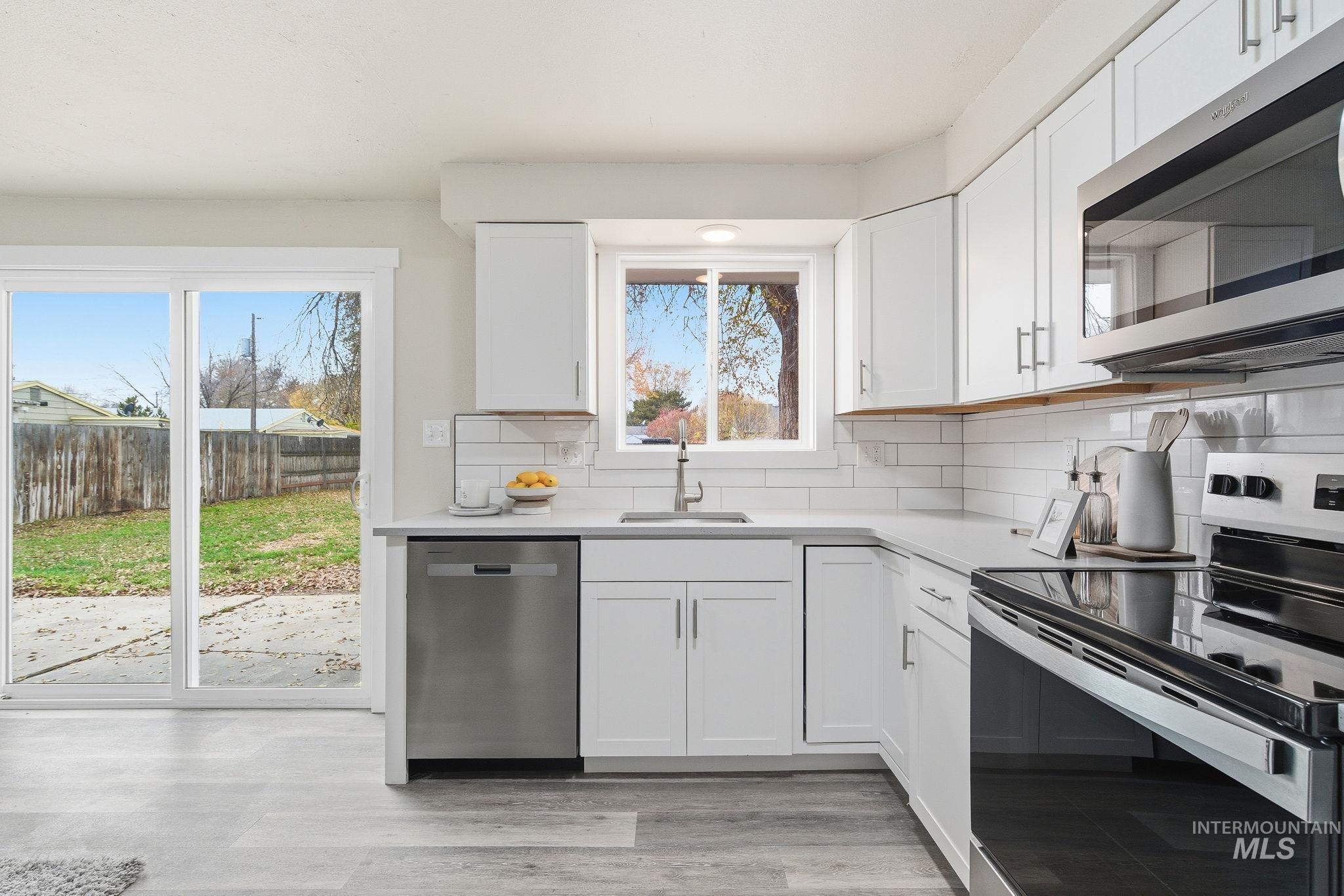 Kitchen featuring stainless steel appliances, backsplash, white cabinets, and light wood-style floors