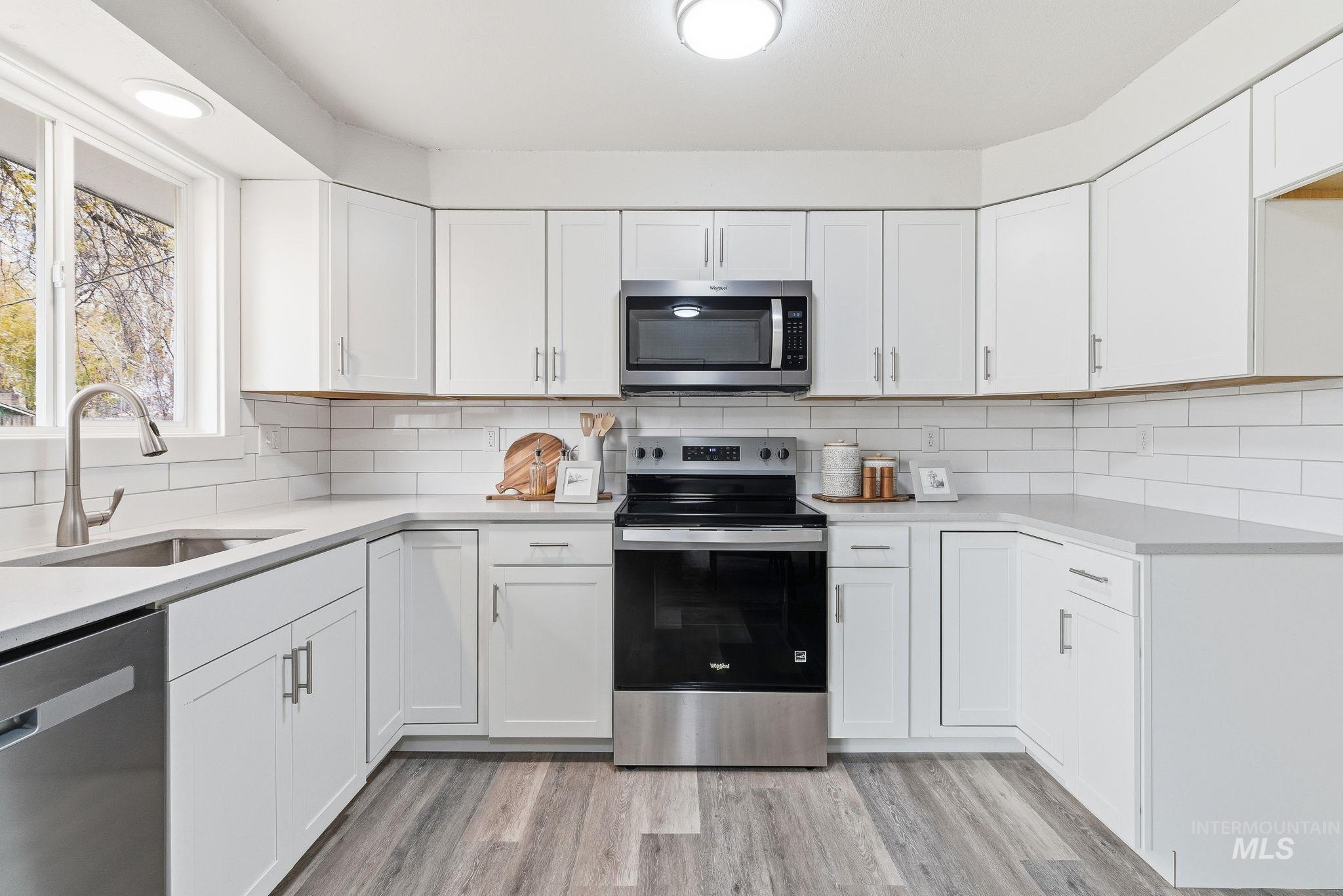 Kitchen with appliances with stainless steel finishes, white cabinetry, light stone countertops, and light wood finished floors