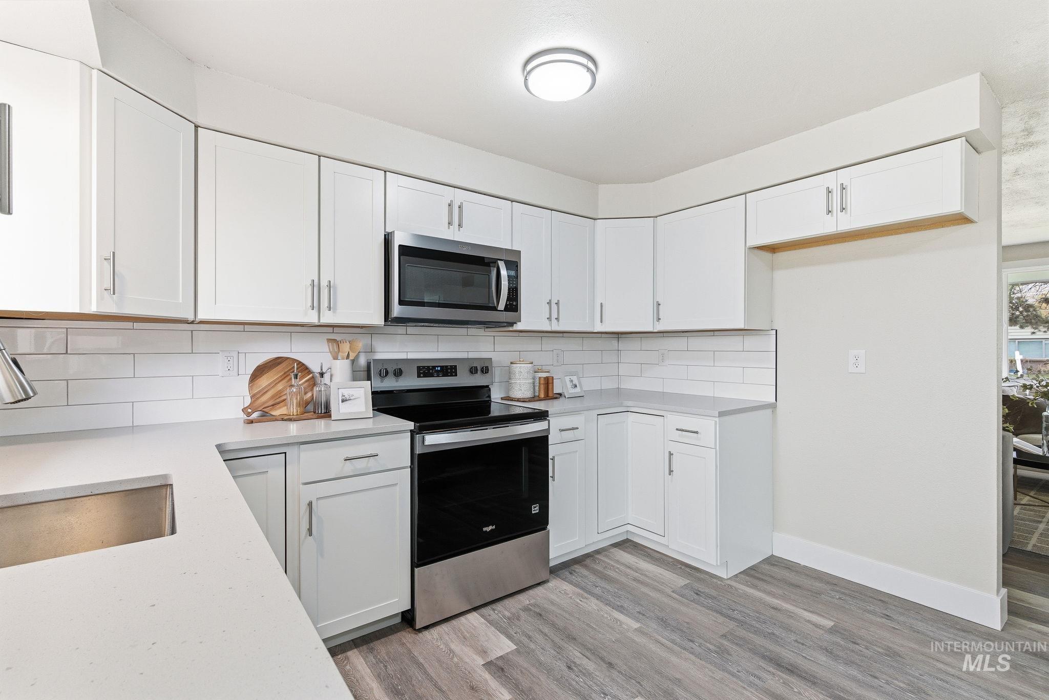 Kitchen featuring stainless steel appliances, white cabinetry, backsplash, and light wood-type flooring