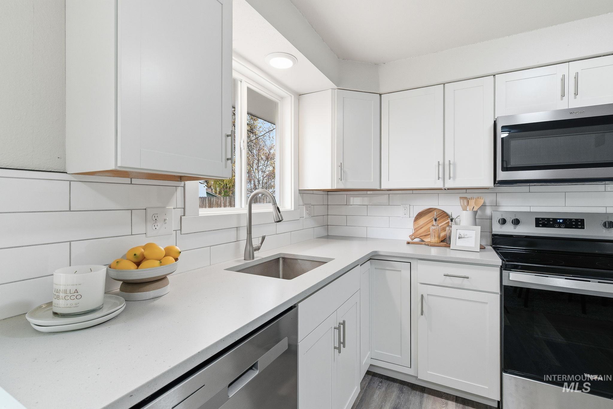 Kitchen featuring appliances with stainless steel finishes, white cabinets, light stone countertops, and decorative backsplash