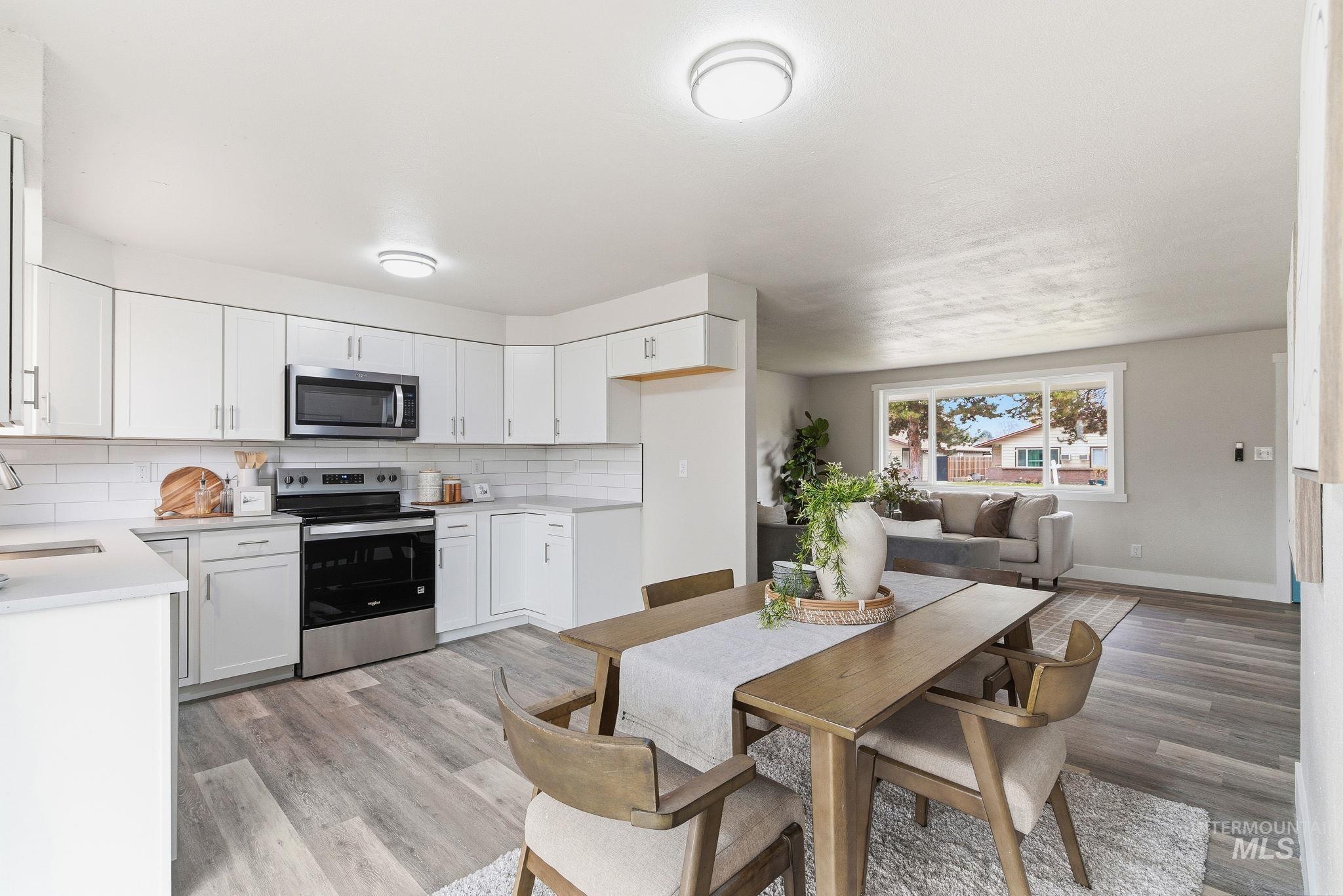 Kitchen featuring appliances with stainless steel finishes, backsplash, white cabinetry, and light wood-style floors