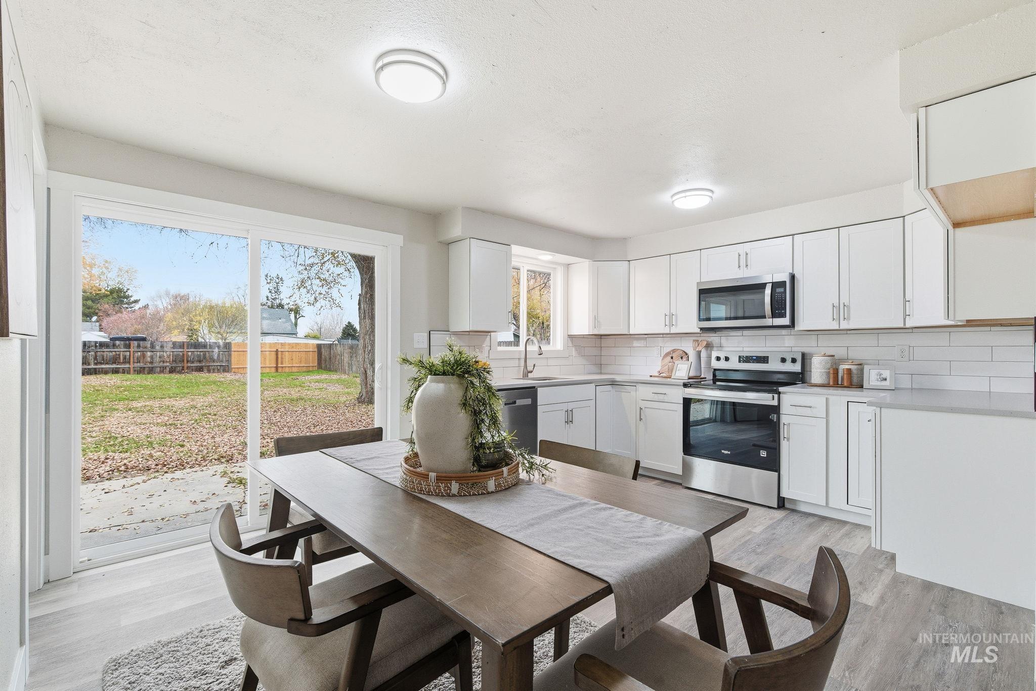 Kitchen featuring stainless steel appliances, light wood finished floors, decorative backsplash, white cabinetry, and light stone countertops