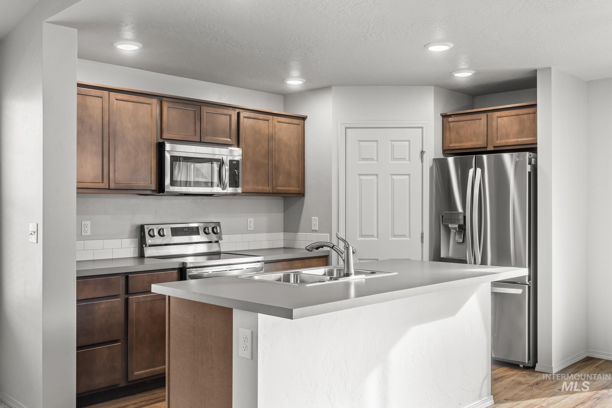 Kitchen with appliances with stainless steel finishes, light wood-style floors, recessed lighting, a center island with sink, and a textured ceiling