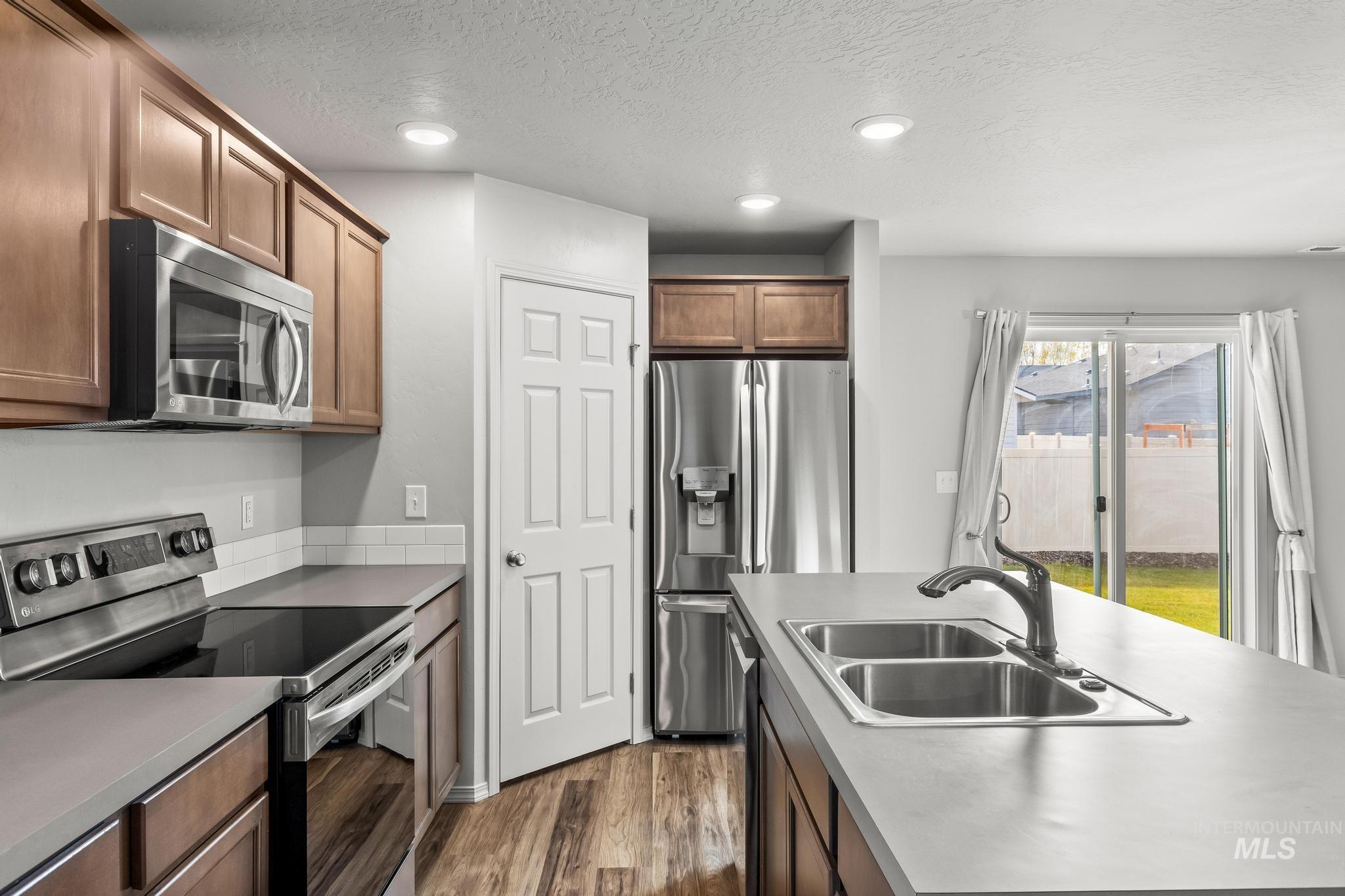 Kitchen with appliances with stainless steel finishes, dark wood-style flooring, a textured ceiling, brown cabinets, and recessed lighting