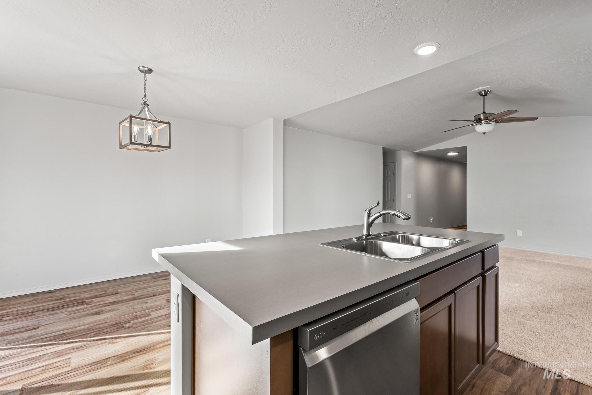 Kitchen featuring a kitchen island with sink, dishwasher, light wood-style floors, pendant lighting, and open floor plan