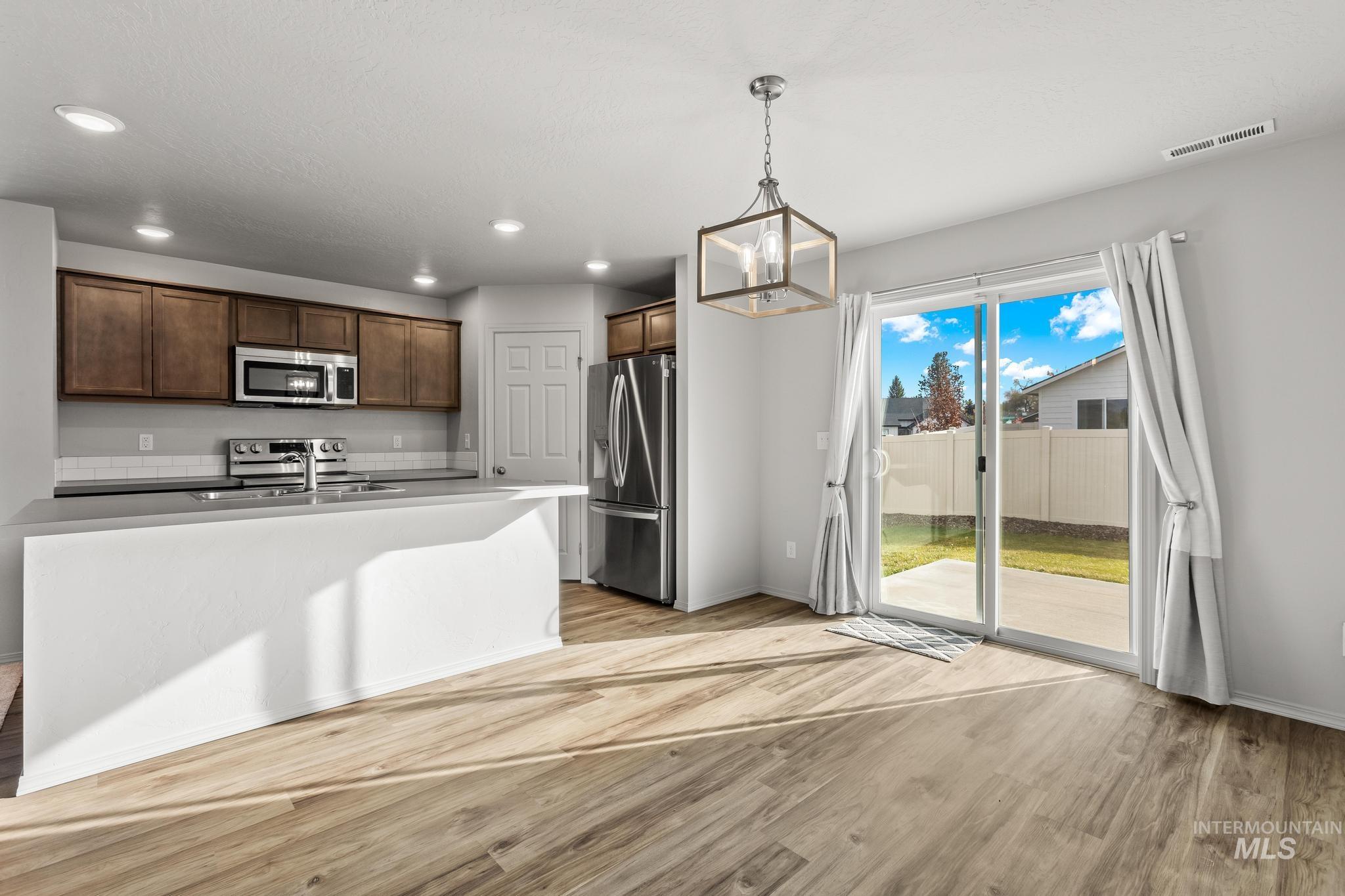 Kitchen with stainless steel appliances, light wood finished floors, hanging light fixtures, dark brown cabinets, and recessed lighting