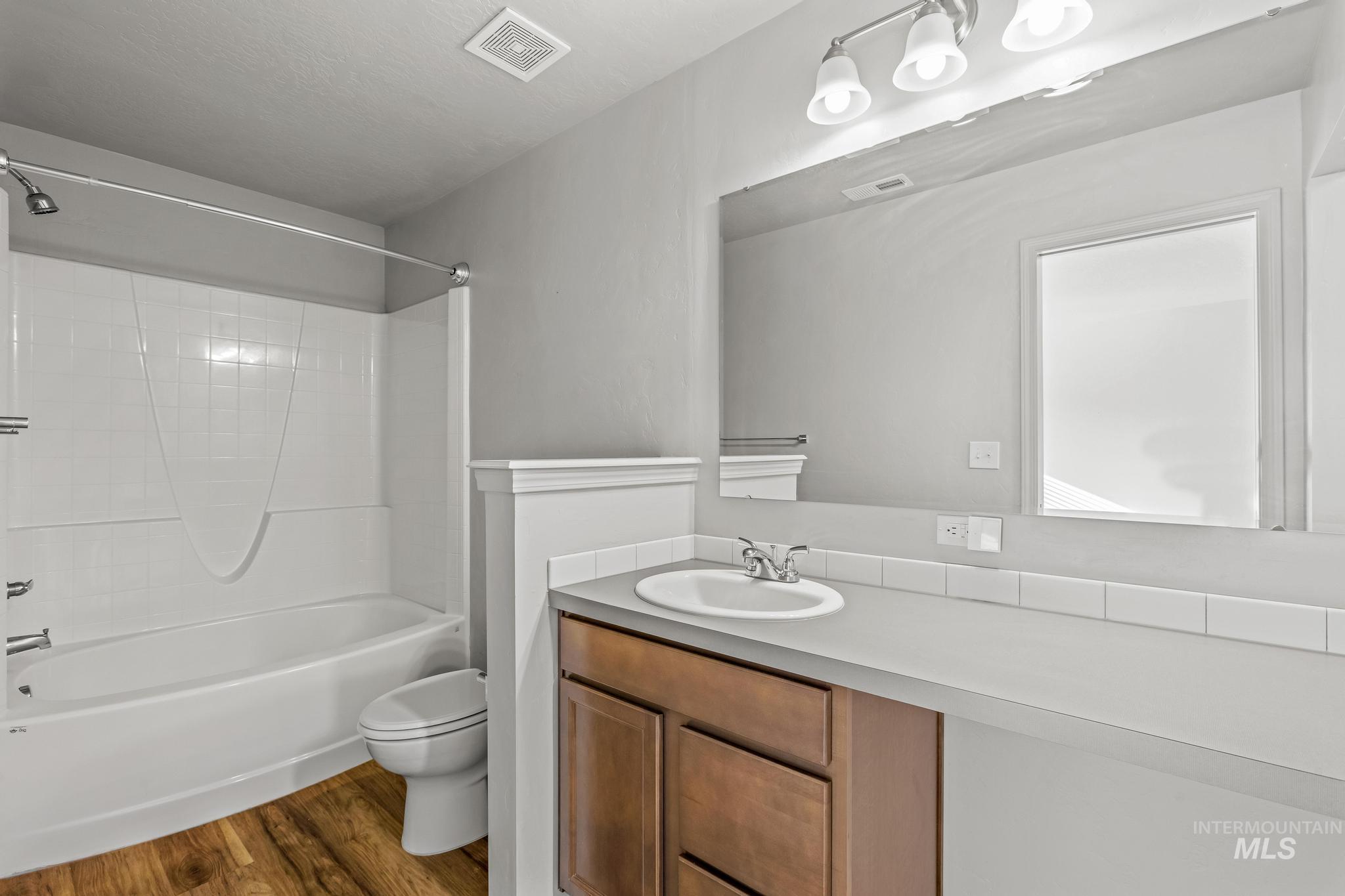 Bathroom with vanity, washtub / shower combination, and dark wood-style flooring
