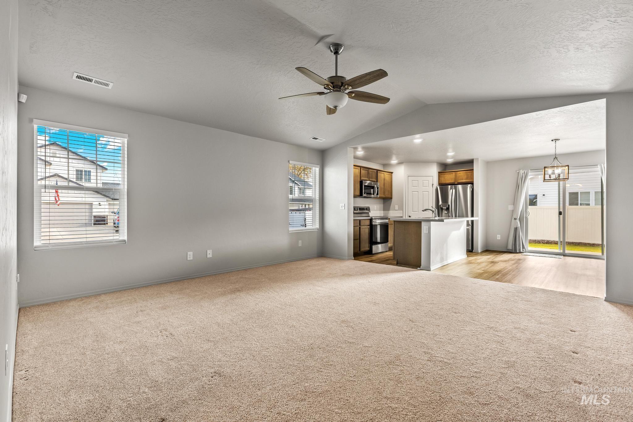 Unfurnished living room with vaulted ceiling, light colored carpet, a ceiling fan, and a textured ceiling