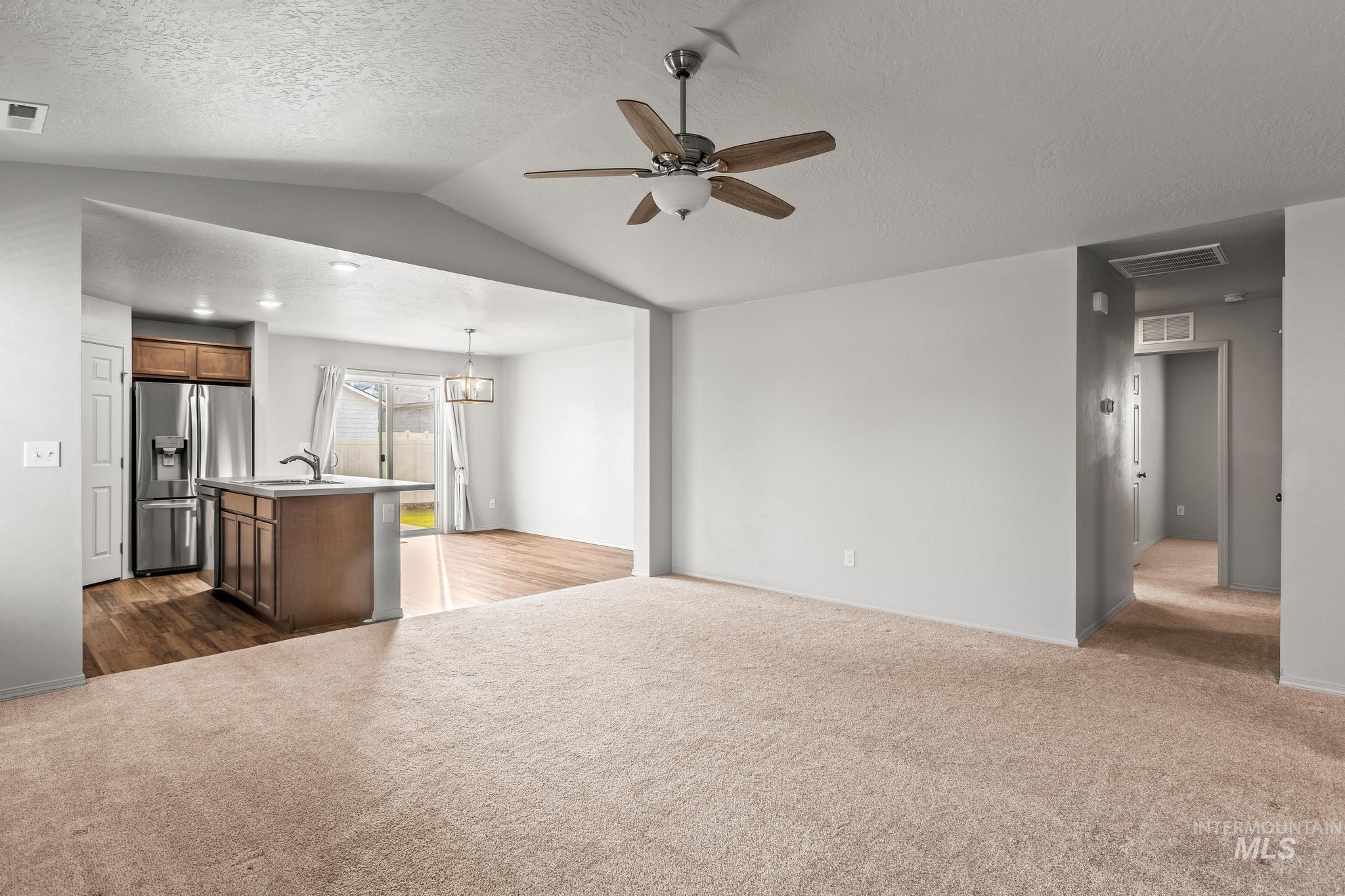 Unfurnished living room with dark carpet, a textured ceiling, vaulted ceiling, and ceiling fan