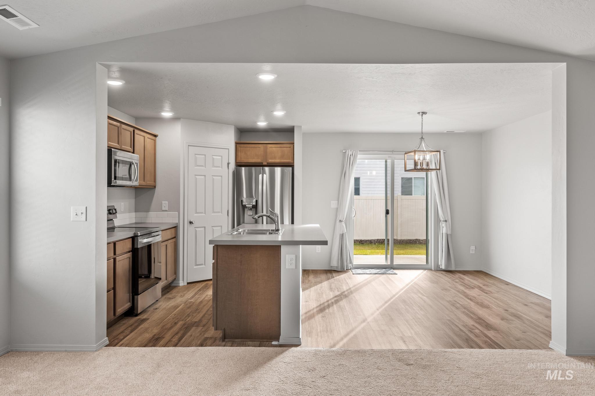 Kitchen with stainless steel appliances, a kitchen island with sink, pendant lighting, a chandelier, and brown cabinetry
