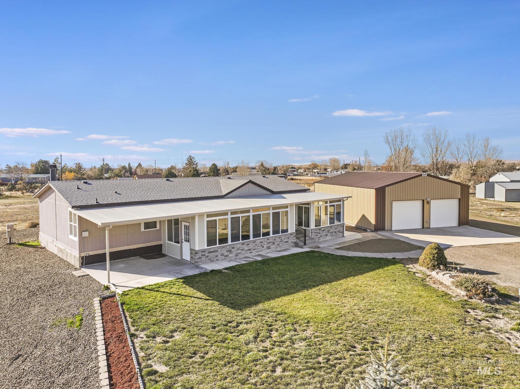 Front view of house with driveway, garage/shop, a lawn, a shingled roof, and a patio area