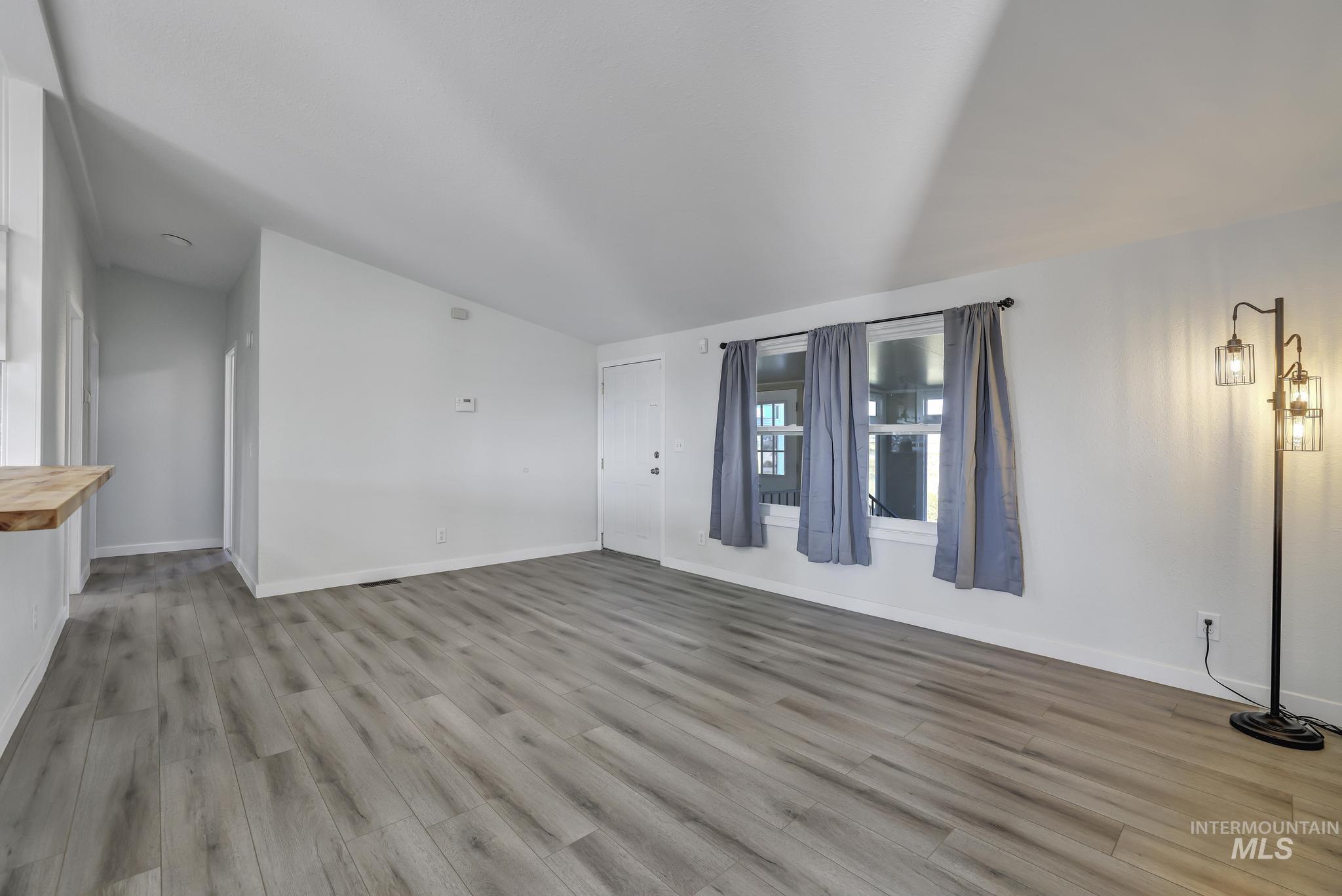 Unfurnished living room with light wood-style floors and vaulted ceiling