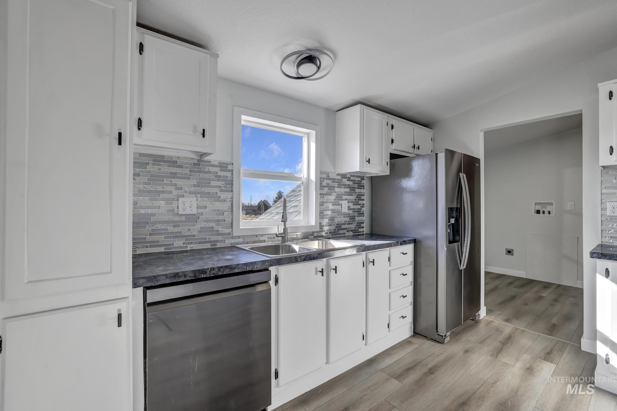 Kitchen featuring dark countertops, decorative backsplash, appliances with stainless steel finishes, white cabinetry, and light wood-type flooring